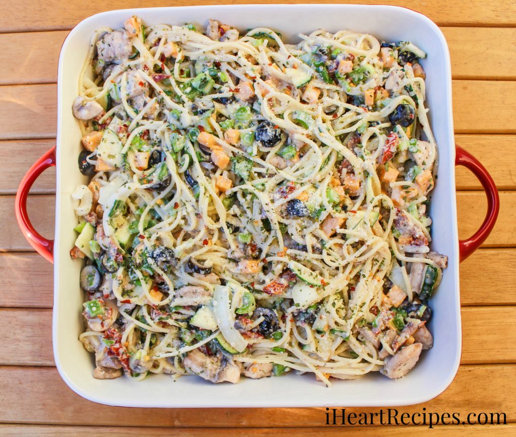 Tender spaghetti pasta and fresh vegetables tossed in a creamy sauce served in a red square serving dish on top of a wooden table. 