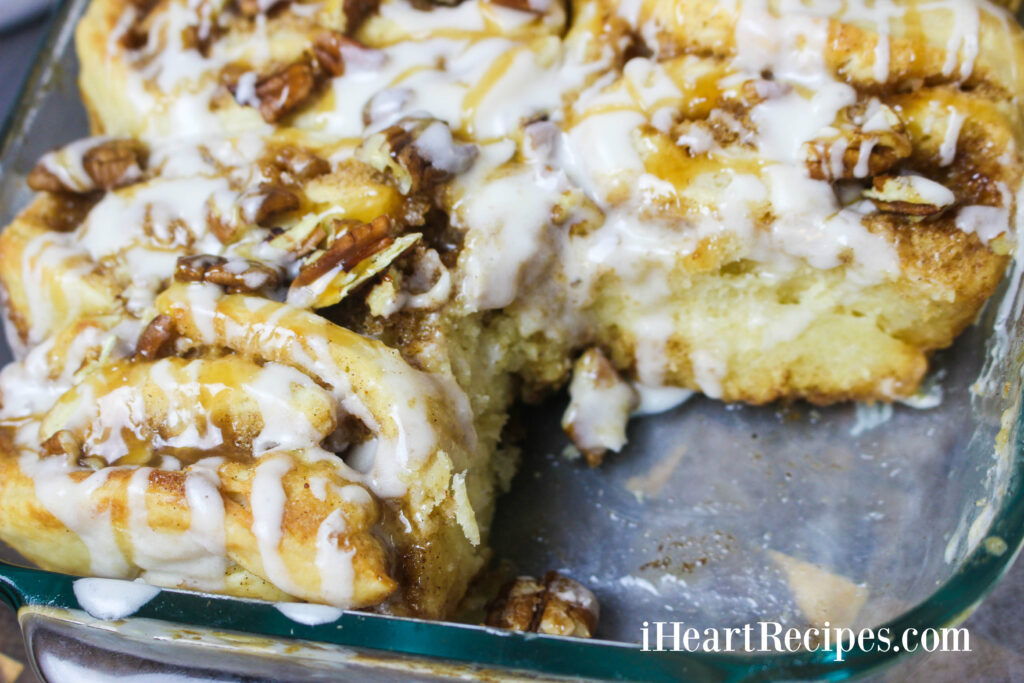 Gooey Caramel Pecan Cinnamon Rolls drizzled with icing and caramel sauce served in a glass baking dish. Nothing beats this made-from-scratch recipe!