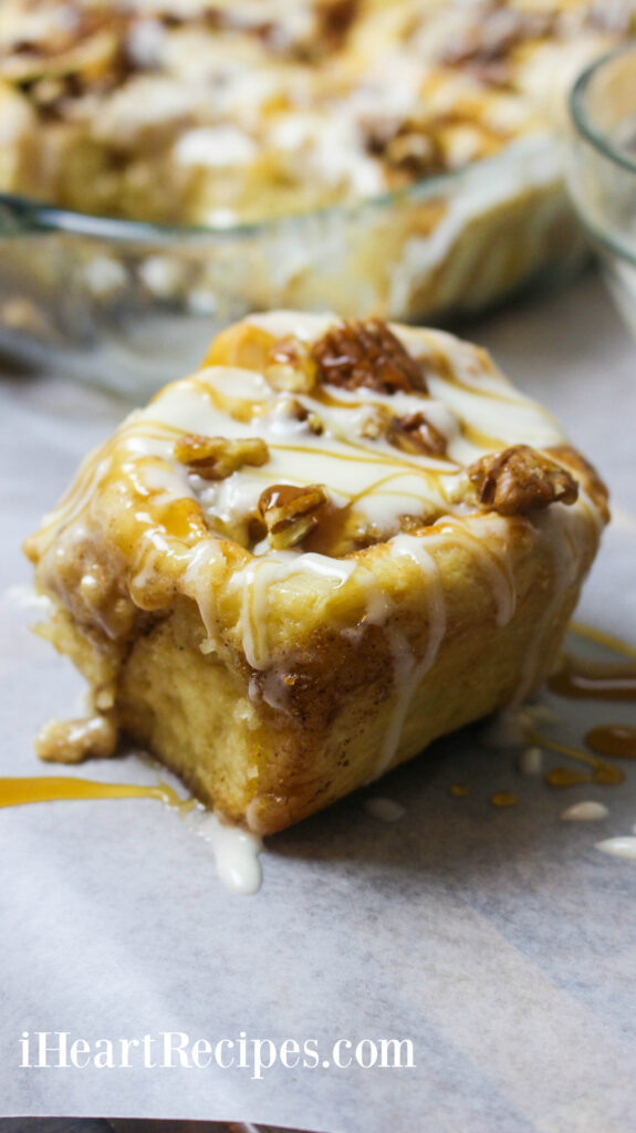 A sweet and gooey Caramel Pecan Cinnamon Roll drizzled with icing and caramel sauce served on parchment paper. 