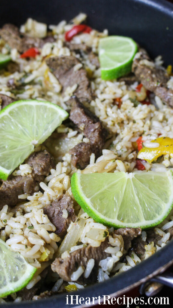 Colorful peppers, tender steak and fluffy rice topped with lime wedges, served in a skillet. 