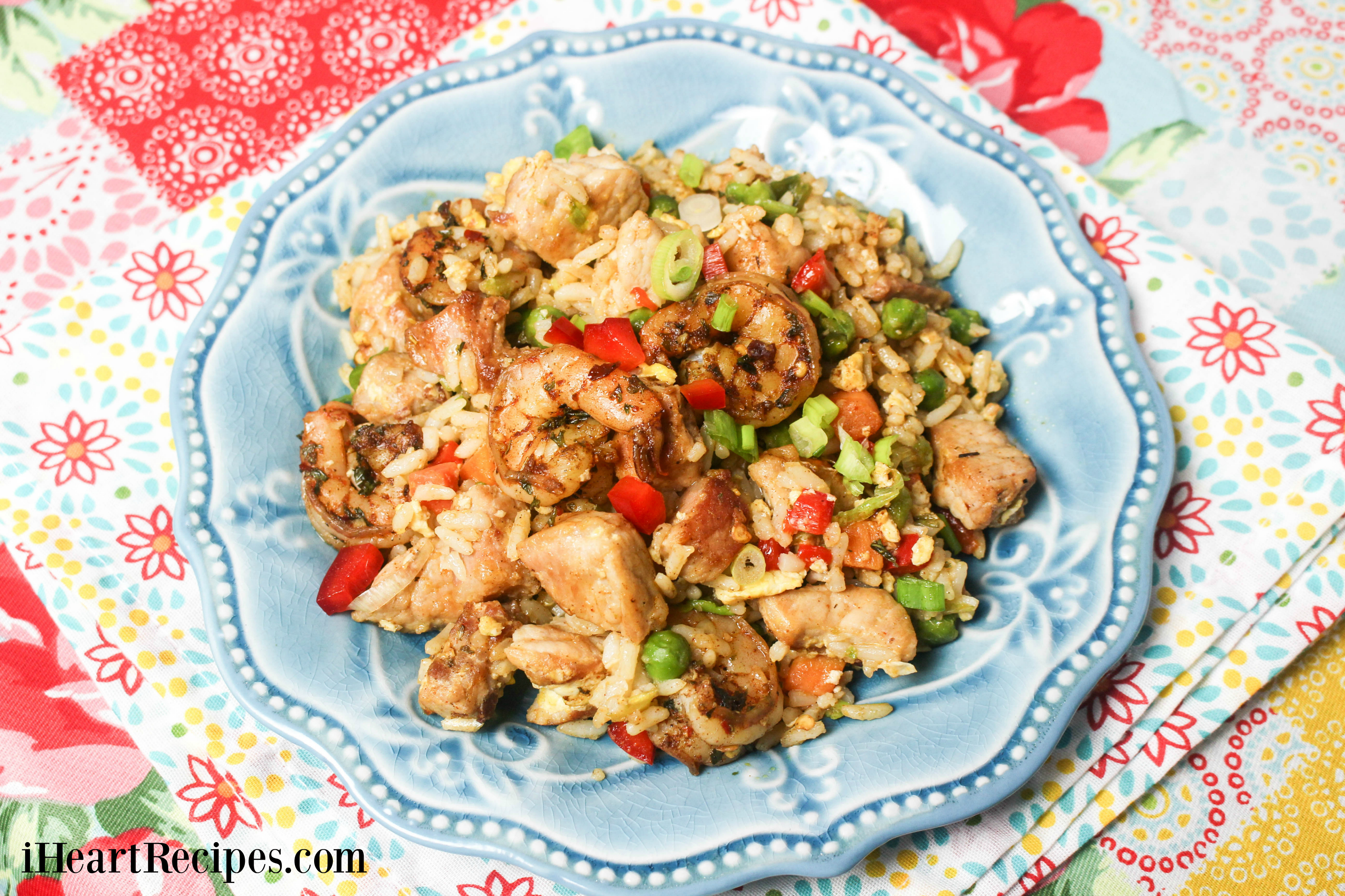 Flavorful Pork & Jerk Shrimp Fried Rice served on a blue scalloped plate on top of a floral tablecloth. 