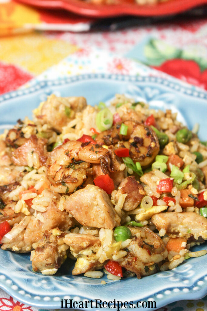 A close-up image of tender Pork & Jerk Shrimp Fried Rice with bright colored veggies served on a blue scalloped plate. 