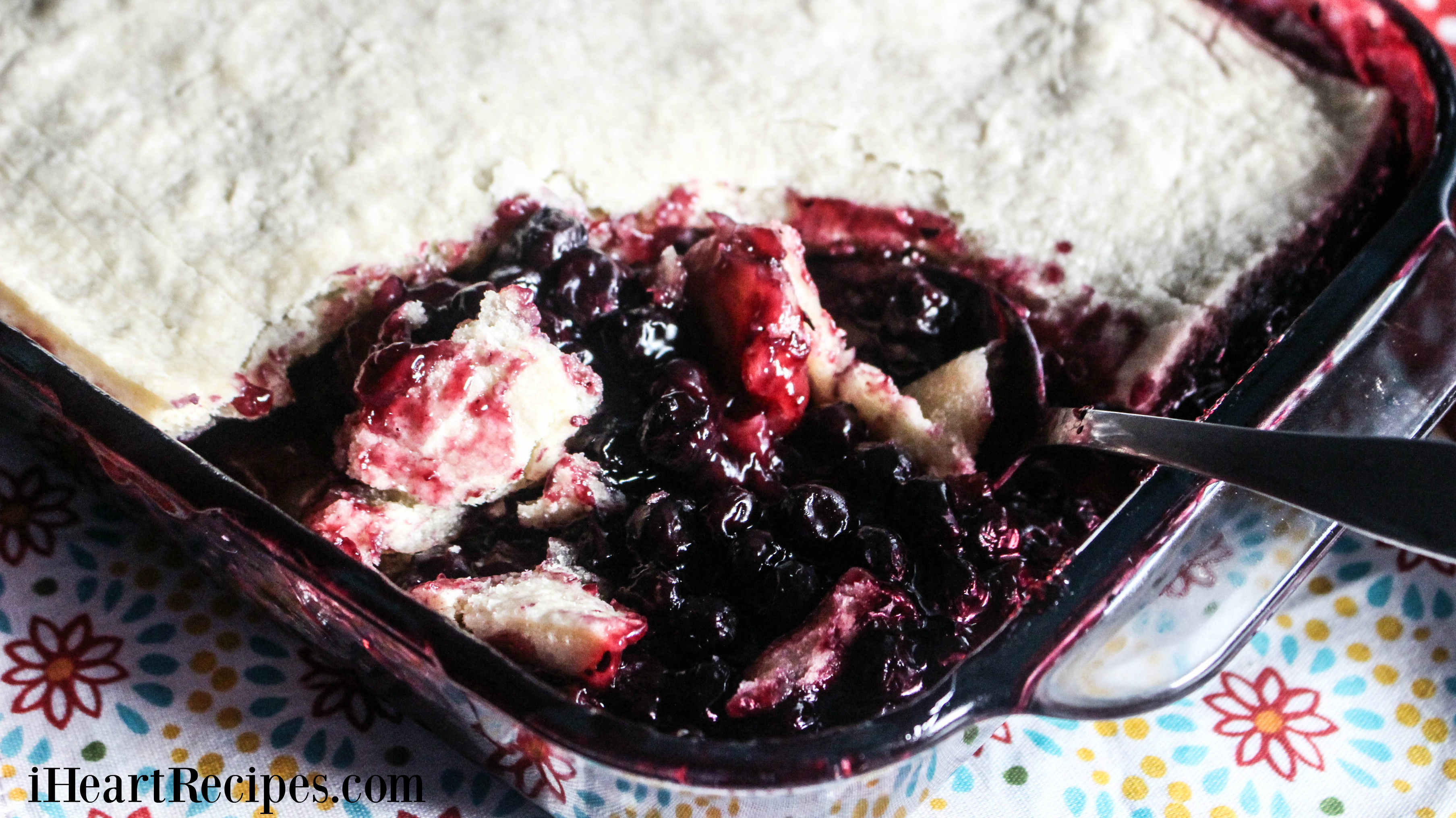 Juicy southern blueberry cobbler topped with a flaky crust being served from a glass baking dish. 