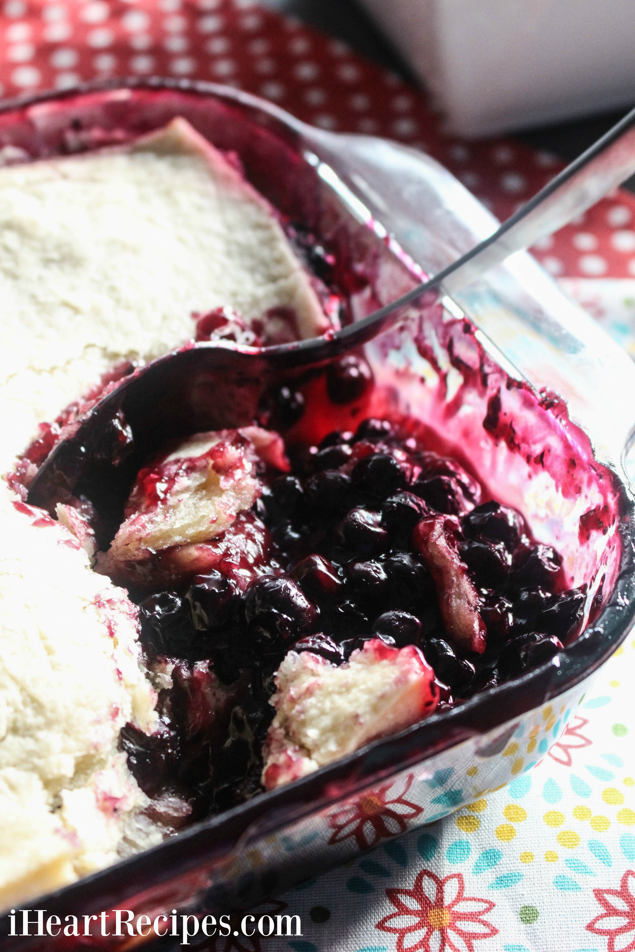 Spoonfuls of sweet blueberry cobbler being served from a classic glass baking dish. 