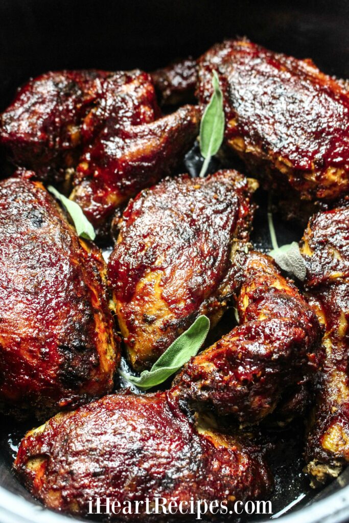 Sweet and tangy BBQ chicken thighs coated in BBQ sauce with fresh basil leaves in a slow cooker pot.