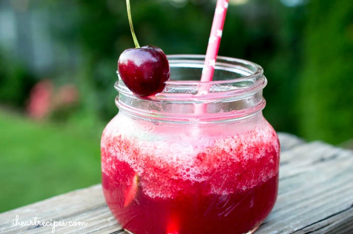 A glass mason jar filled with sweet Cherry Lime Vodka Slushie, served with a paper straw and bright red cherry. This will be a hit at your next pool-side party!