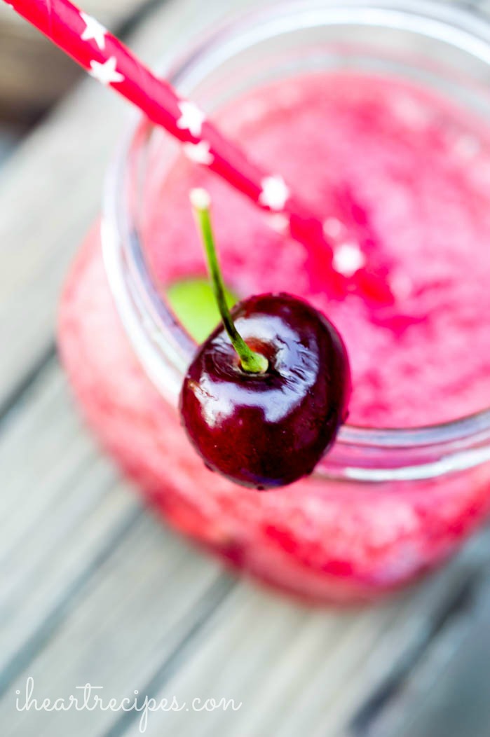 A Cherry Lime Vodka Slushie served in a glass mason jar and garnished with a bright red cherry. It's the perfect sweet treat on a hot day! 