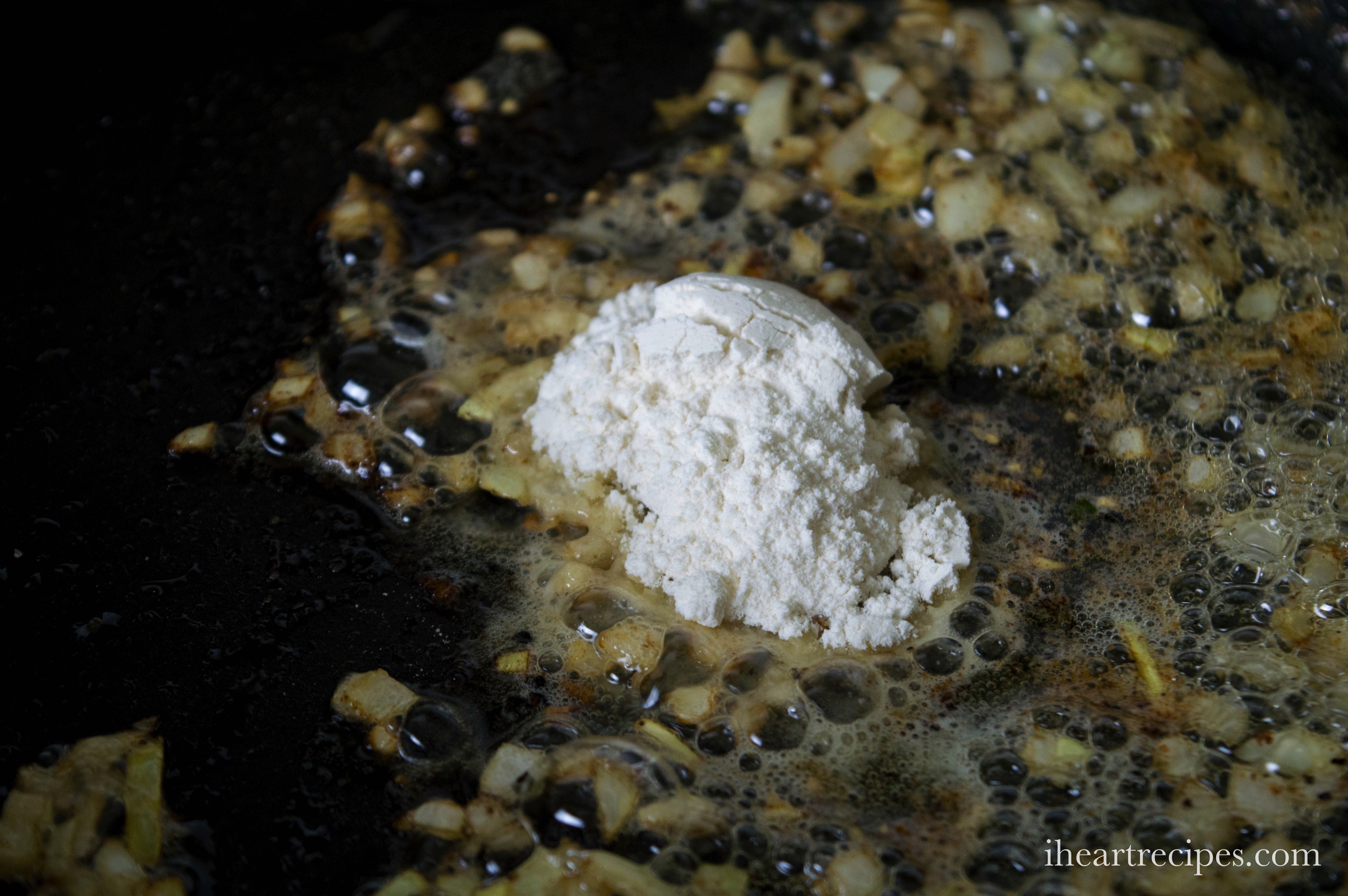 A spoonful of all-purpose flour sits in a skillet with diced onions sauteed in butter.