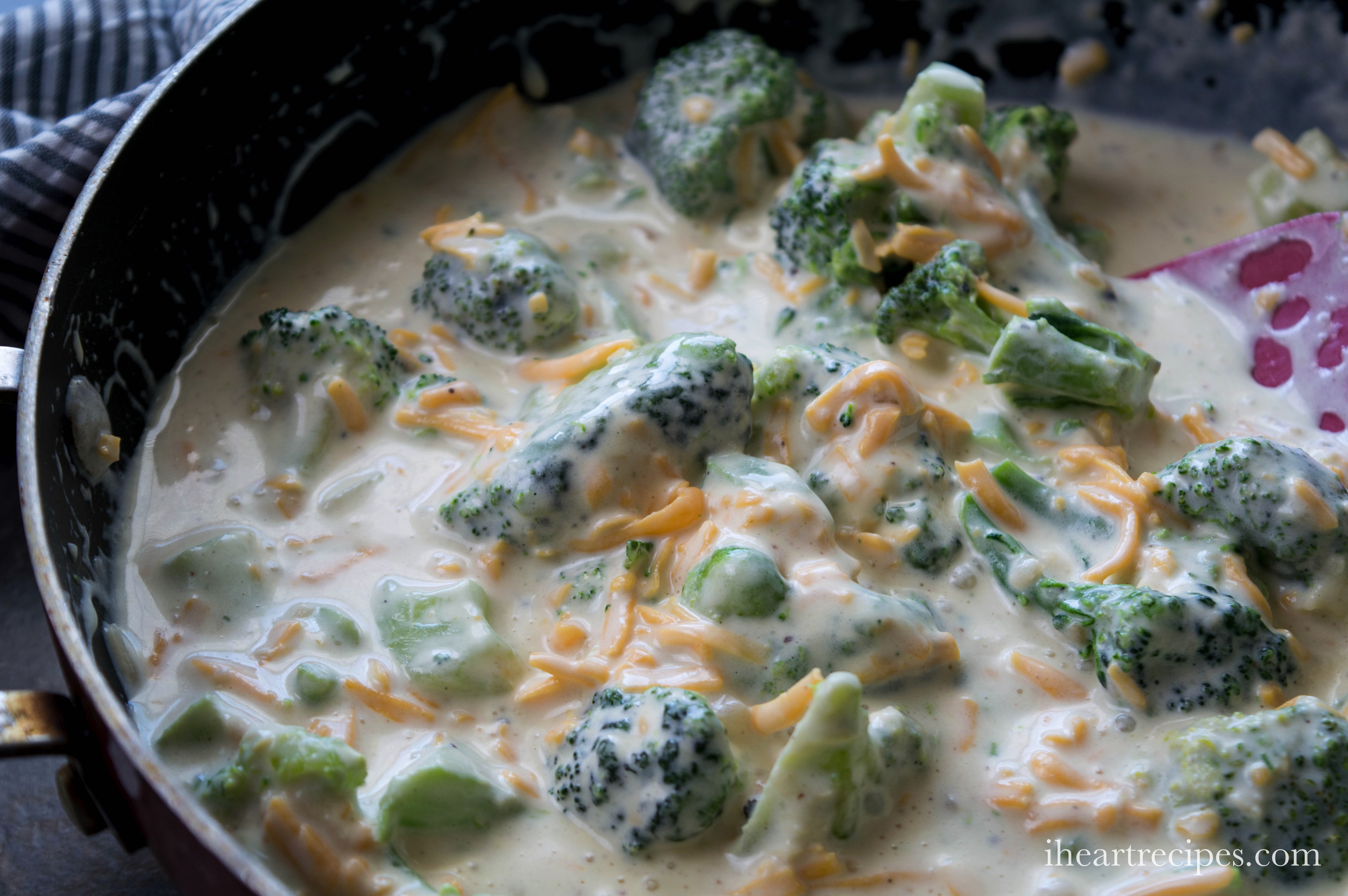 A creamy mixture of broccoli florets and shredded cheese in a creamy sauce resting in a skillet.