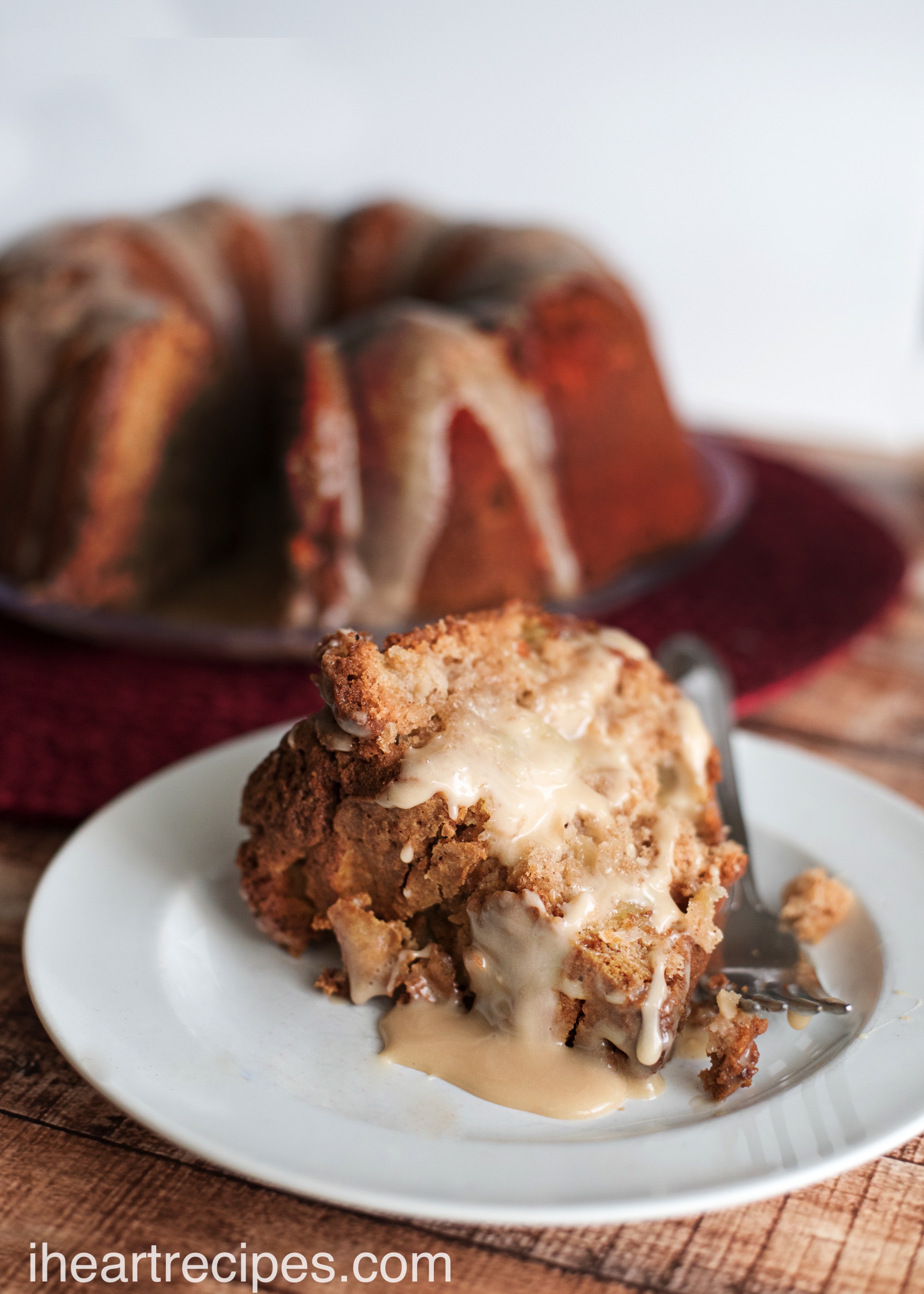 A slice of tasty apple cake drizzled with sweet maple glaze on a classic white plate ready to be served. This cake is full of autumn goodness! 