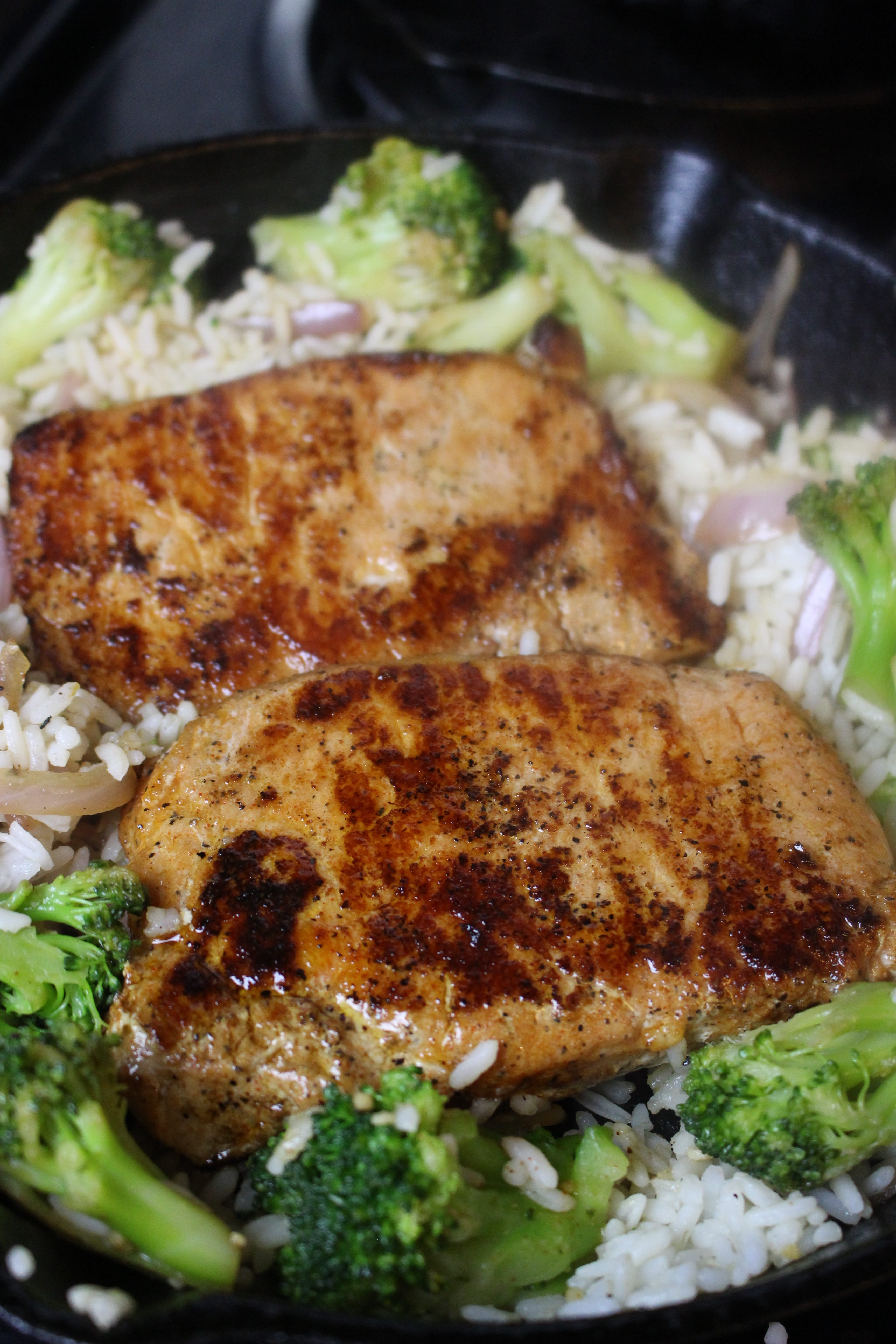 Seasoned pork chops on a bed of tender rice and broccoli served in a cast iron skillet. A terrific family meal!