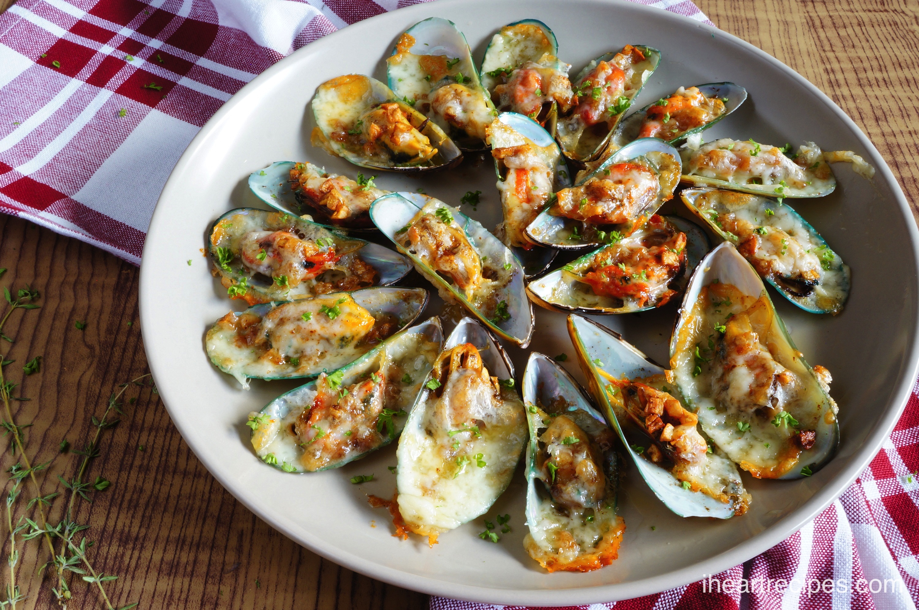 Divine Cheesy Garlic Mussels in a garlicky butter sauce served on a white plate placed on a red and white checkered tablecloth and rustic wooden table. 