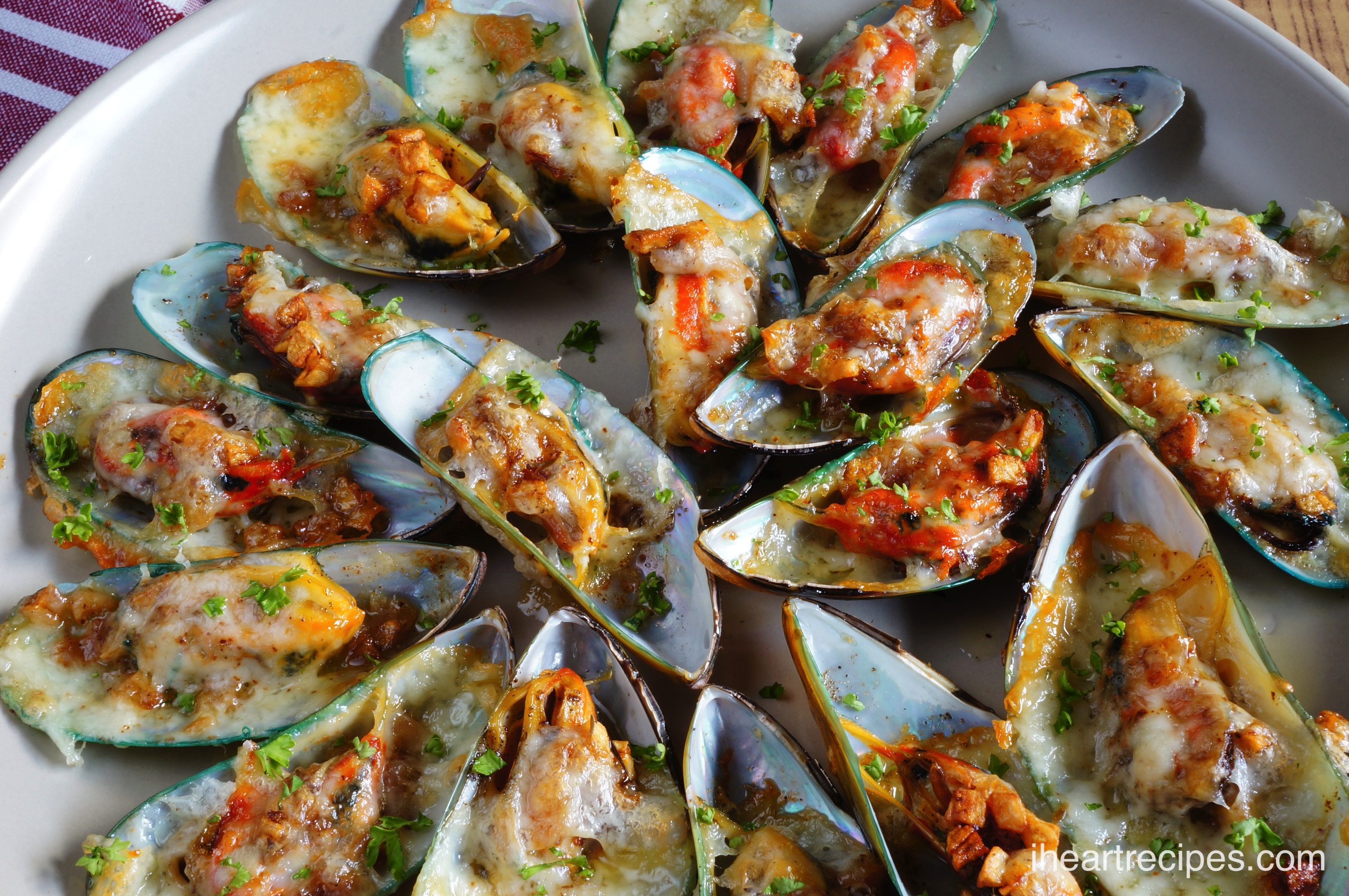 Tender Cheesy Garlic Mussels garnished with bright green parsley served on a classic white platter.