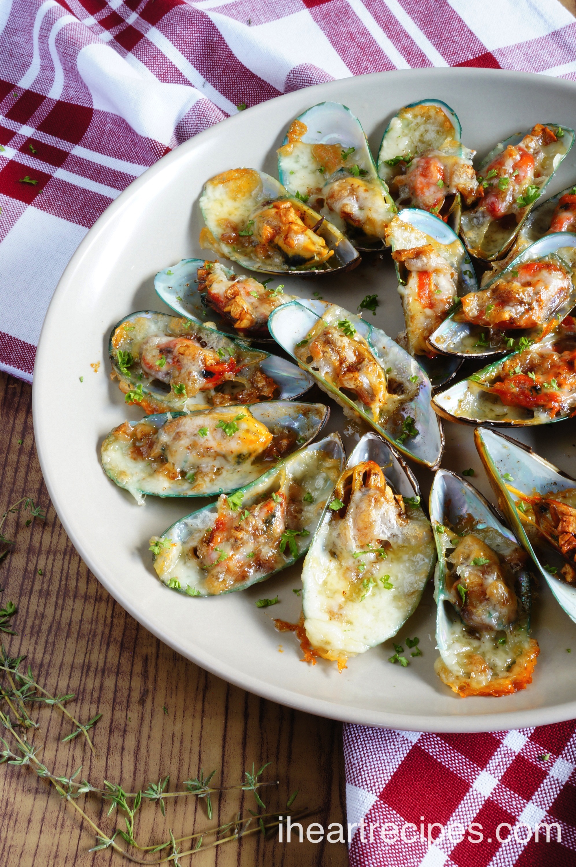 Mouth-watering Cheesy Garlic Mussels served on a simple white plate on top of a red and white checkered cloth set on a rustic wooden table.