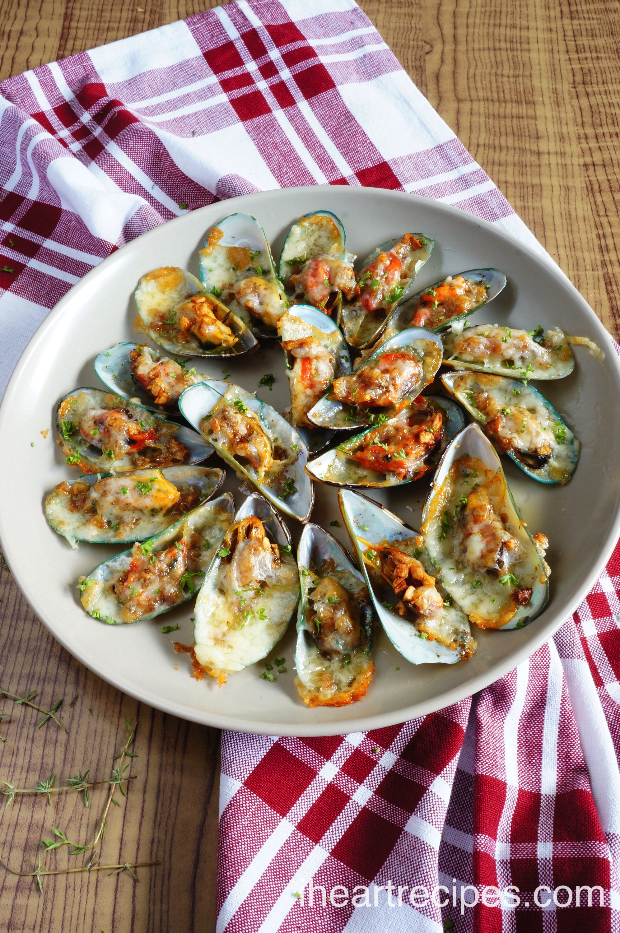 Cheesy Garlic Mussels arranged on a round white plate set on a red and white checkered cloth atop a rustic wooden table. Serve these irresistible mussels as an appetizer, side, or with pasta. 