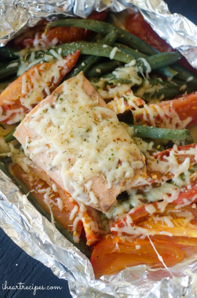 A close up image of a salmon filet baked with Parmesan cheese and vegetables in a foil pack.