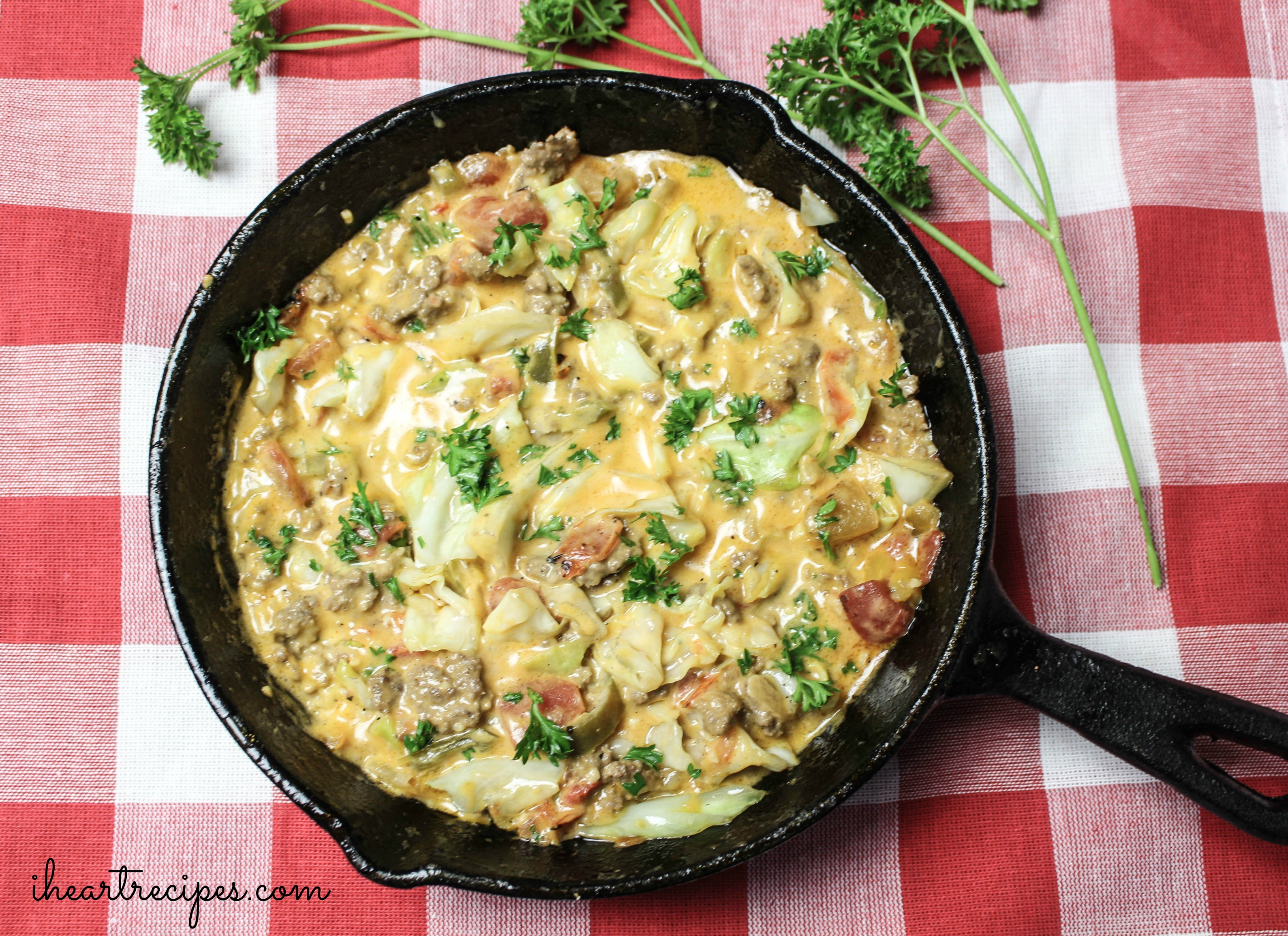 Creamy Cheesy Cabbage Creole topped with fresh green parsley served in a cast iron skillet on top of a red and white checkered tablecloth. This meal is full of flavor and budget-friendly! 