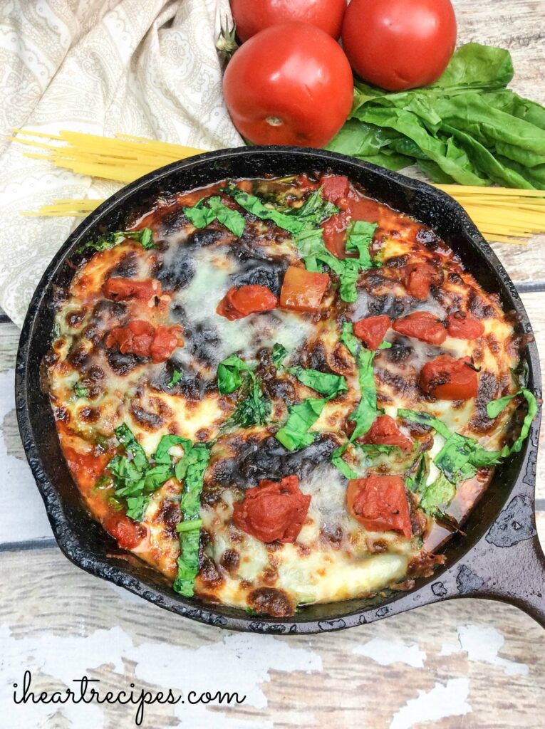 A one-pot chicken parmesan recipe made with breaded chicken, marinara sauce, and cheese, topped with shredded basil in a cast iron skillet.