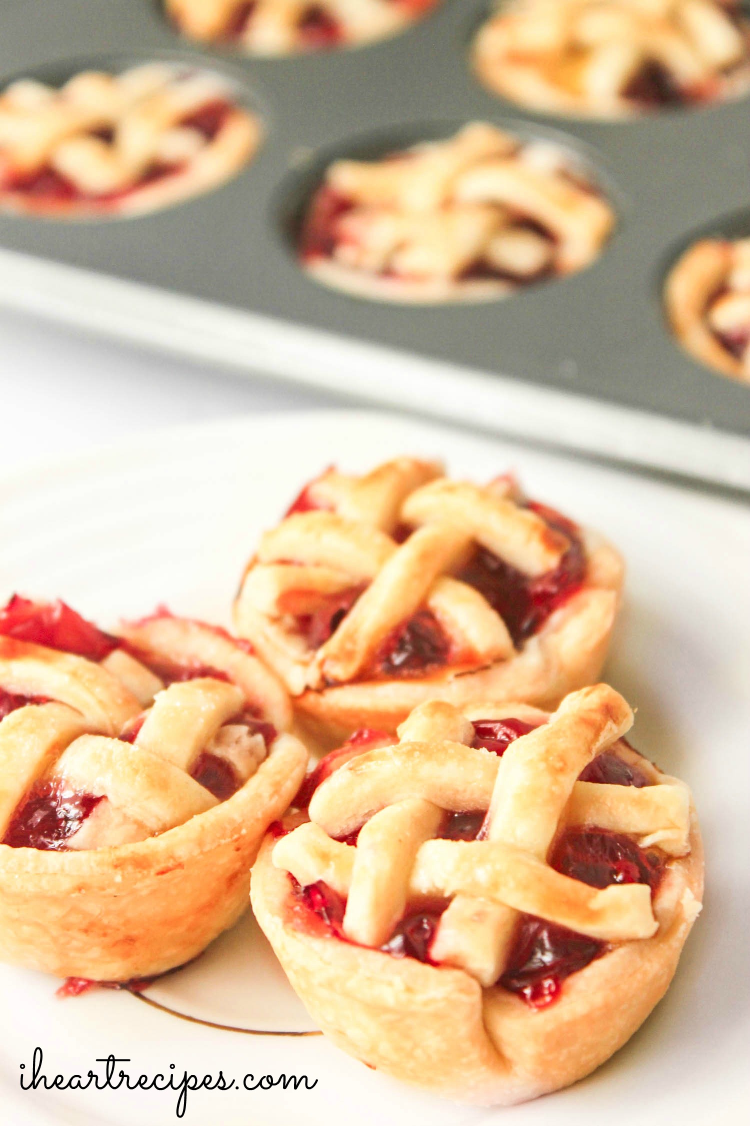 Golden and sweet cherry pie bites served on a white plate. Tangy cherries and a flaky pie crust makes these bite-sized pies the perfect little treat!