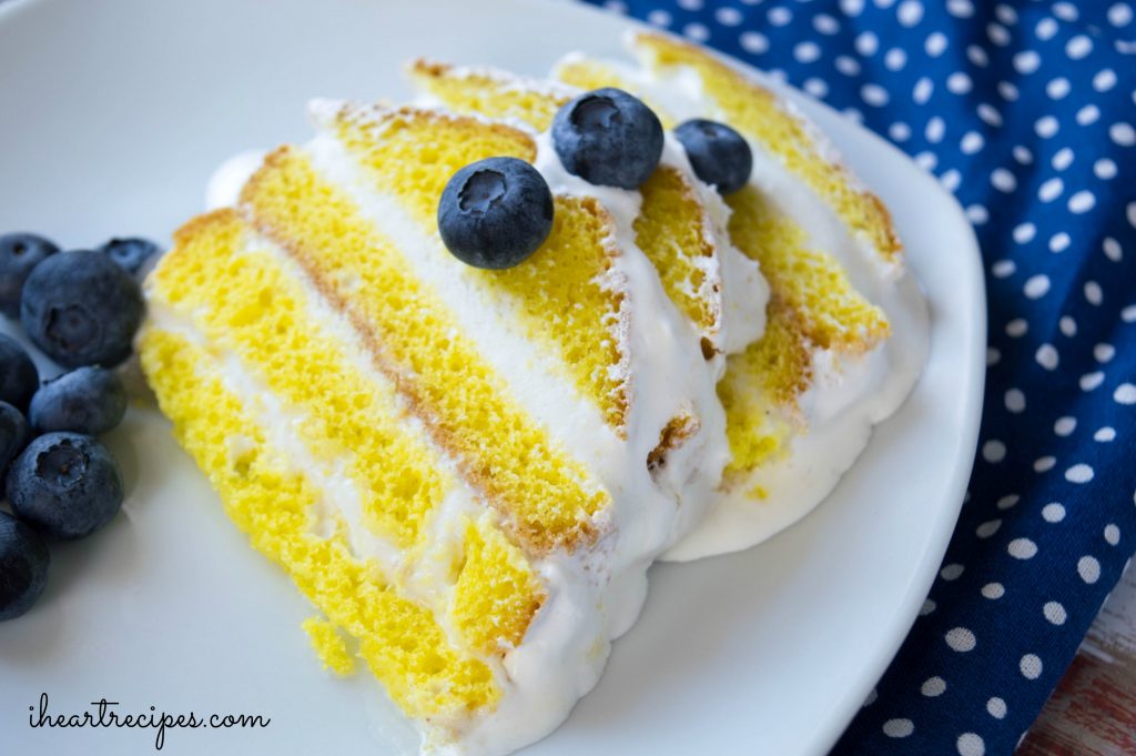 Layered lemon ice cream cake topped with fresh blueberries on a white plate. This dessert is a sweet and refreshing treat that's perfect for summer!