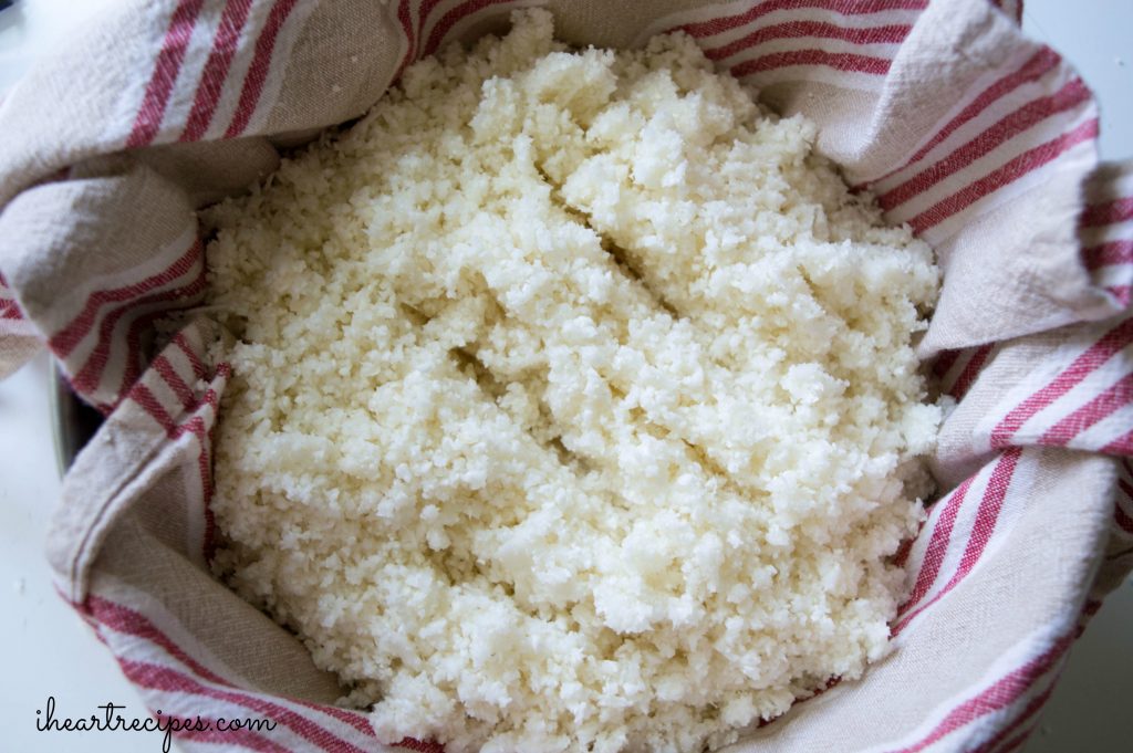 Riced cauliflower in a stainer lined with a red and white striped tea towel.