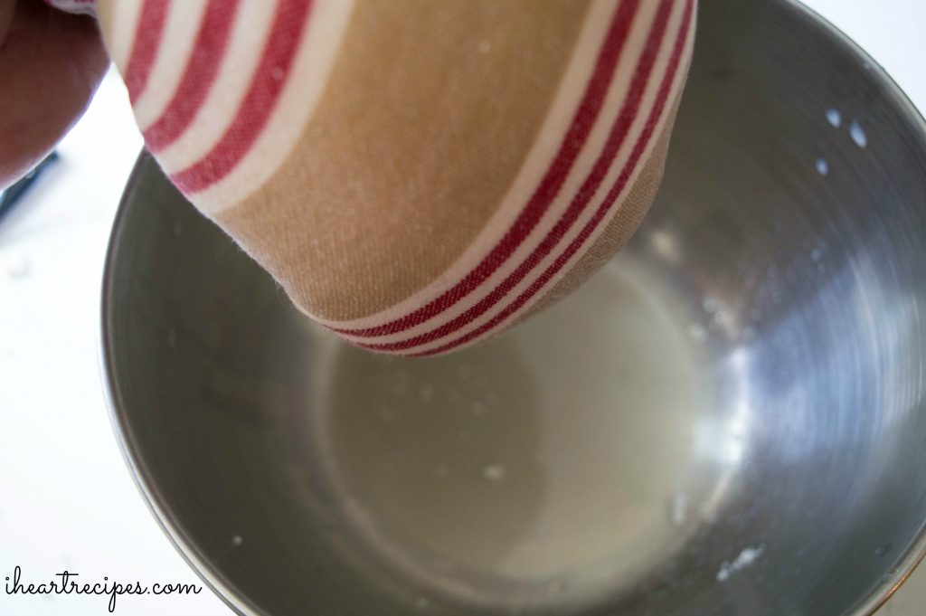 A red, tan and white striped tea towel filled with riced cauliflower being strained into a silver bowl. 