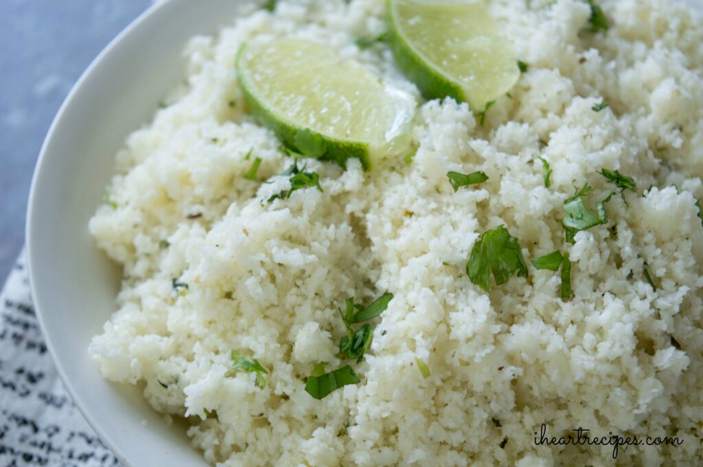 A white dish filled with tender riced cauliflower garnished with cilantro and lime wedges. 