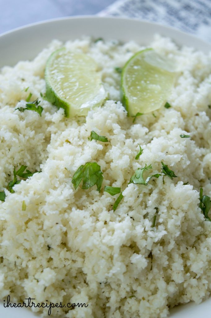 A white dish filled with riced cauliflower garnished with lime wedges and fresh cilantro. 