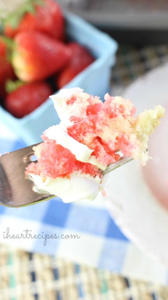 A bite of Strawberry Jello Poke Cake layered with moist yellow cake, strawberry swirls and whipped cream.