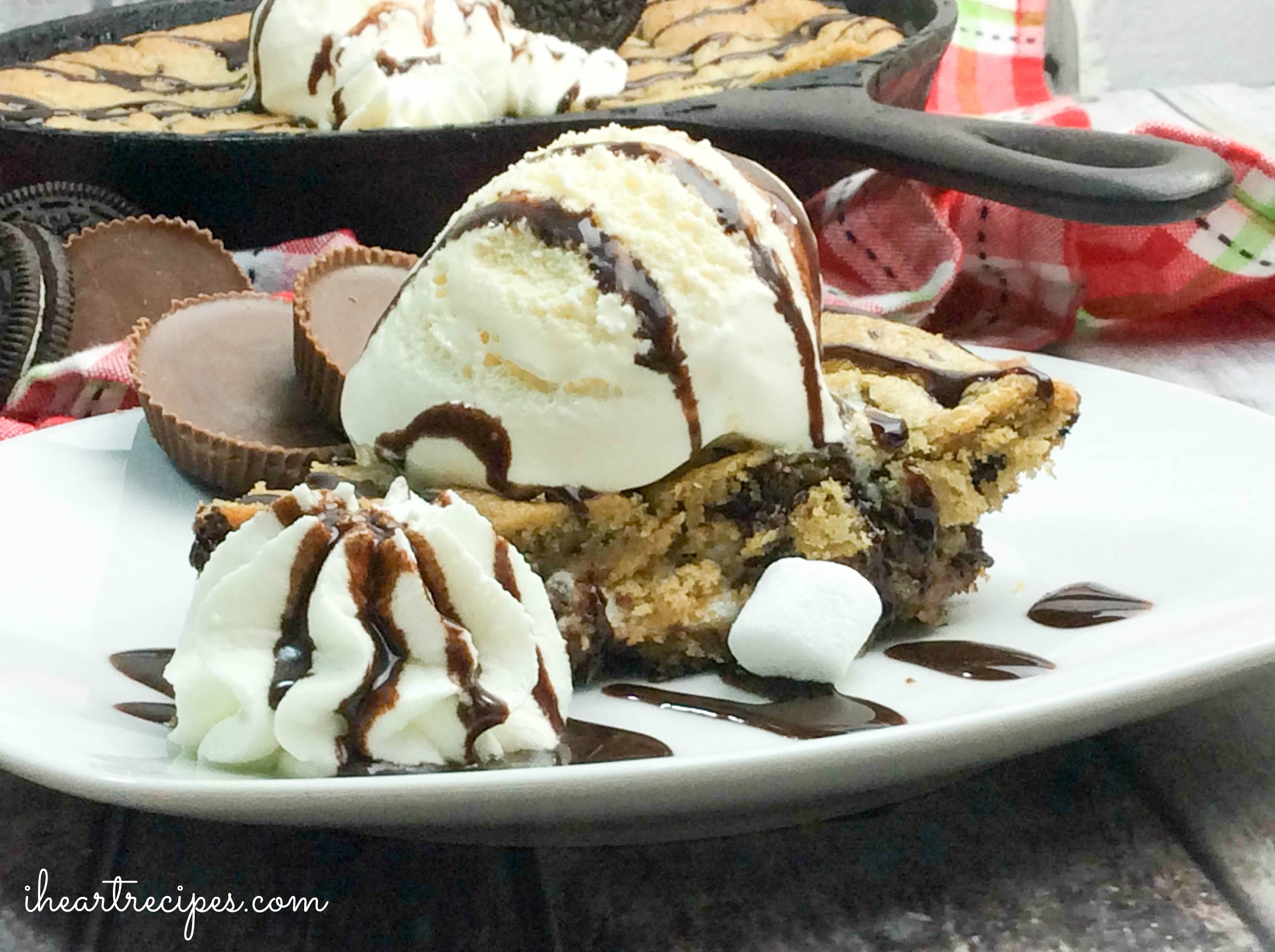 A Delicious Deep Dish Oreo & Reese's Skillet Cookie topped with creamy ice cream and whipped cream drizzled with sweet chocolate syrup on a white plate. A sweet treat!