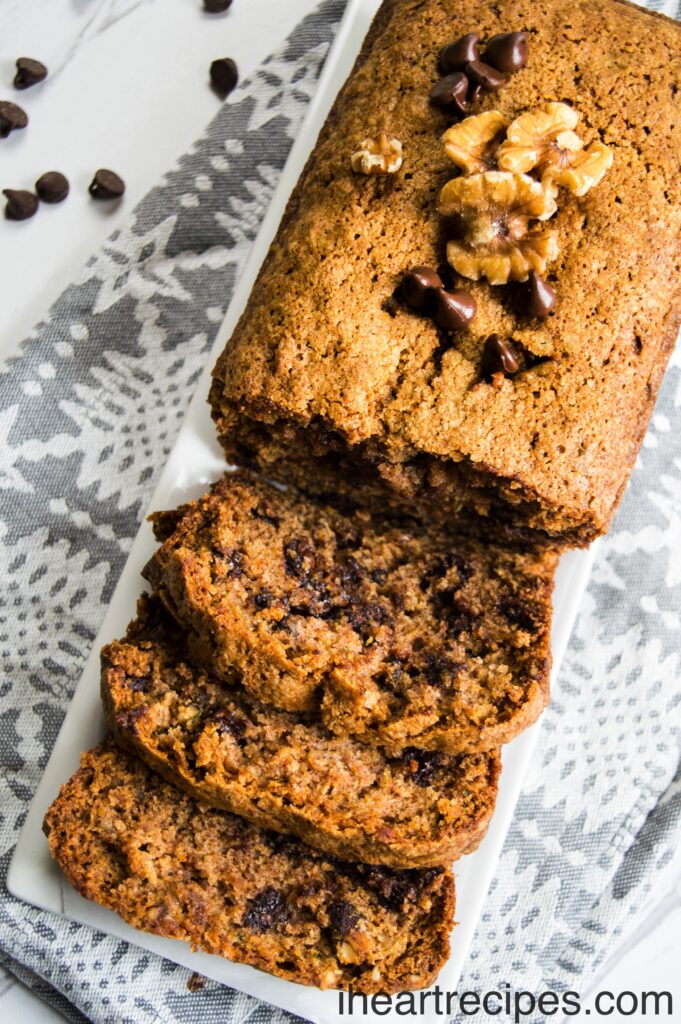 Warm zucchini bread topped with crunchy walnuts and sweet chocolate chips served on a long white platter. Enjoy this delicious treat!