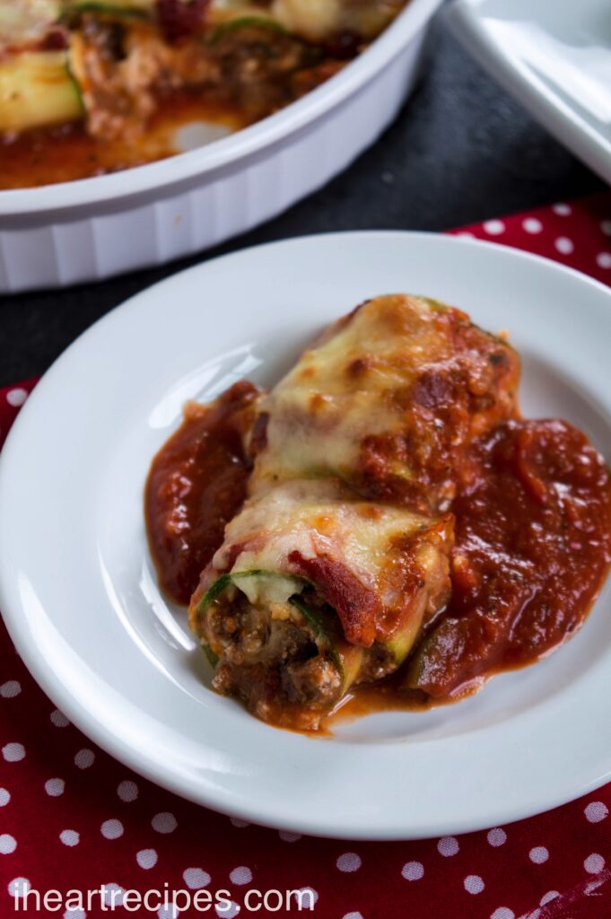 Savory filling wrapped in tender zucchini served on a bed of marinara sauce served on a white plate.