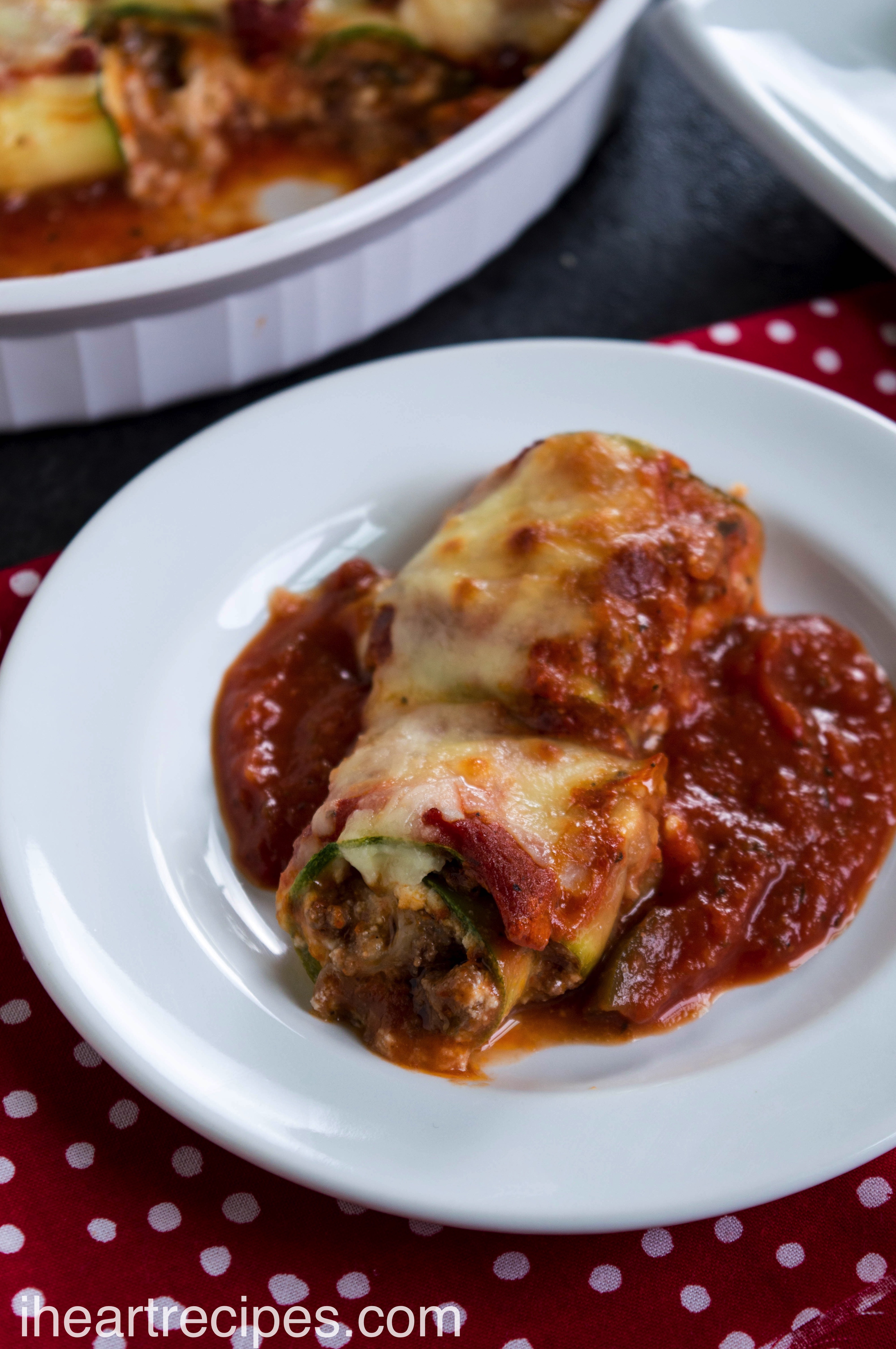 Savory filling wrapped in tender zucchini served on a bed of marinara sauce served on a white plate. 