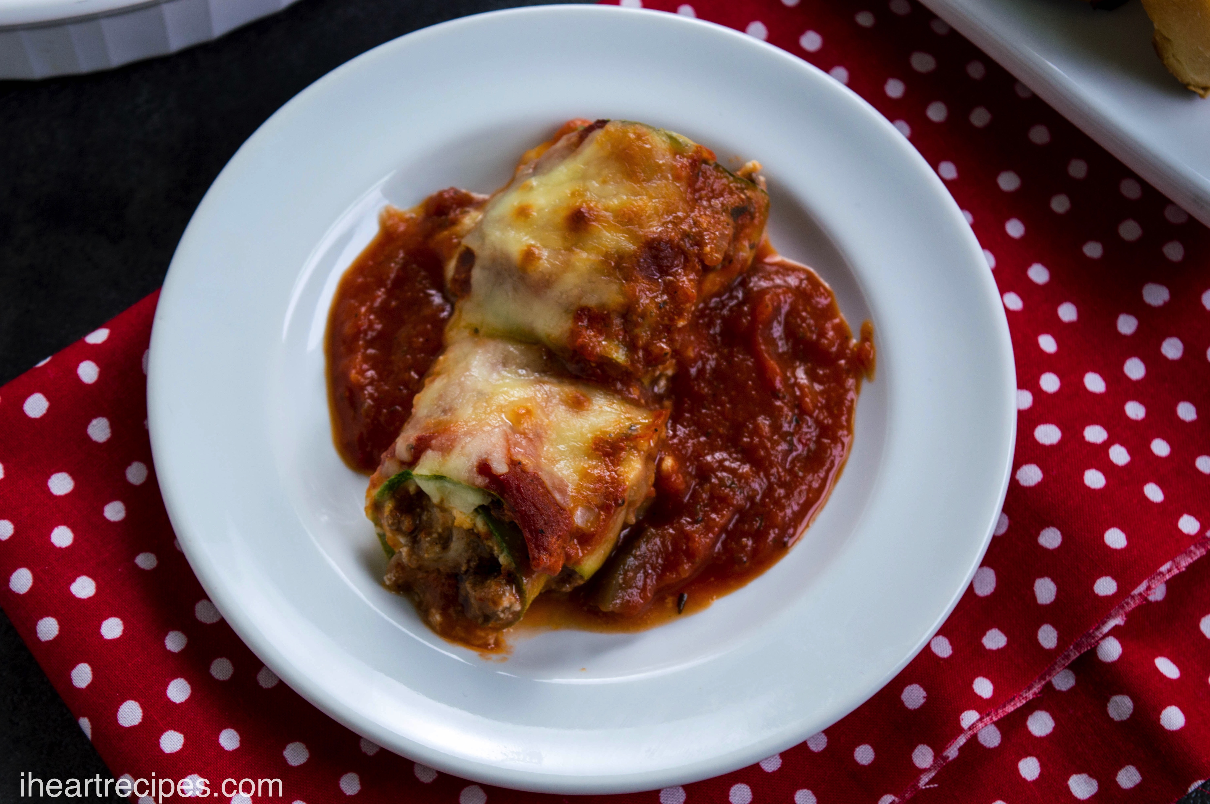 Savory zucchini stuffed with tender beef and creamy ricotta, topped with tangy cheese and served on a bed of hearty marinara sauce, is presented on a white platter.