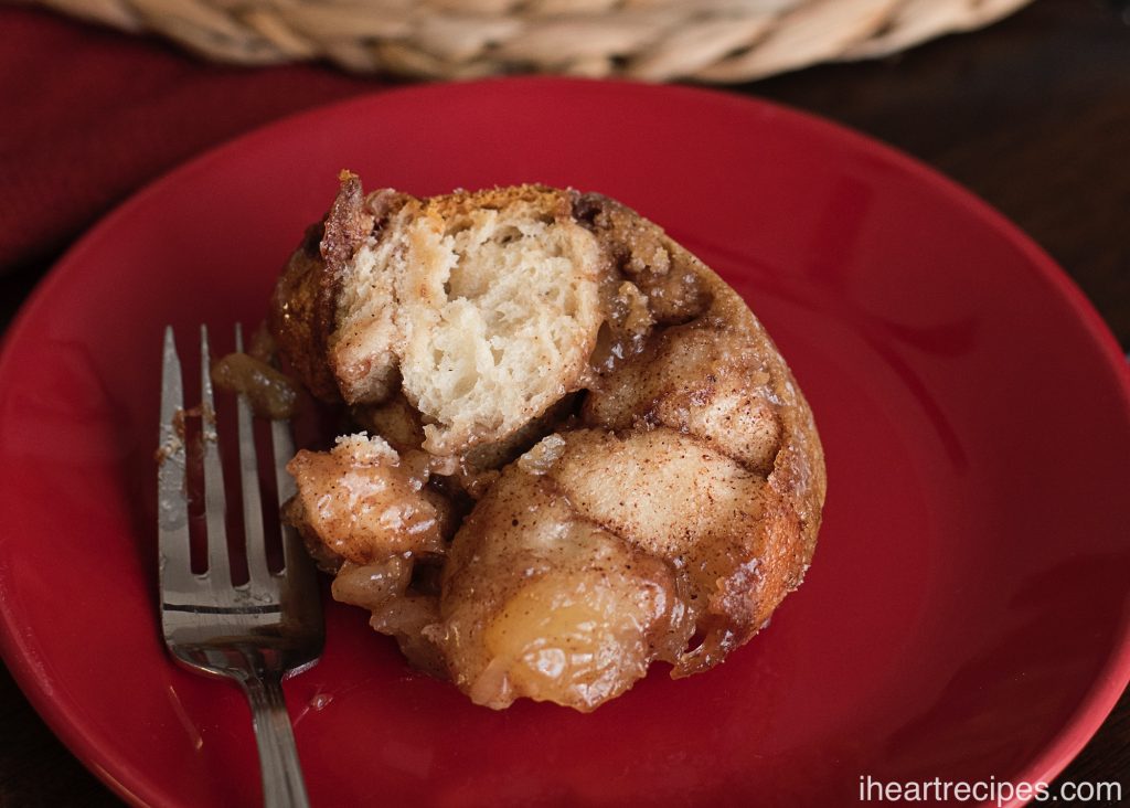 A slice of delicious cinnamon apple pie monkey bread next to a silver fork on a red plate. 