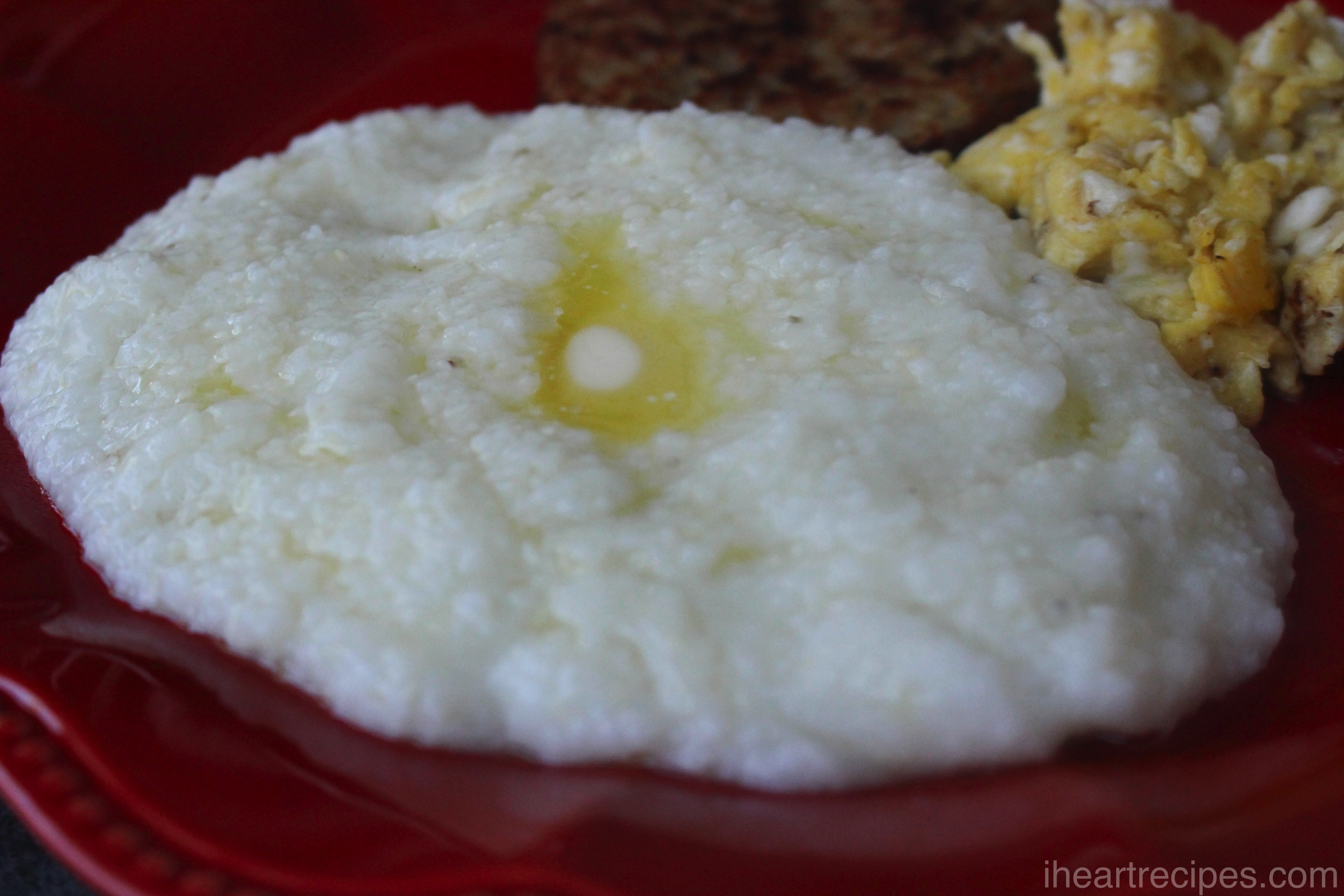 Creamy grits topped with melted butter served on a bright red plate. Serve with savory sausage and tender eggs for a classic southern breakfast!