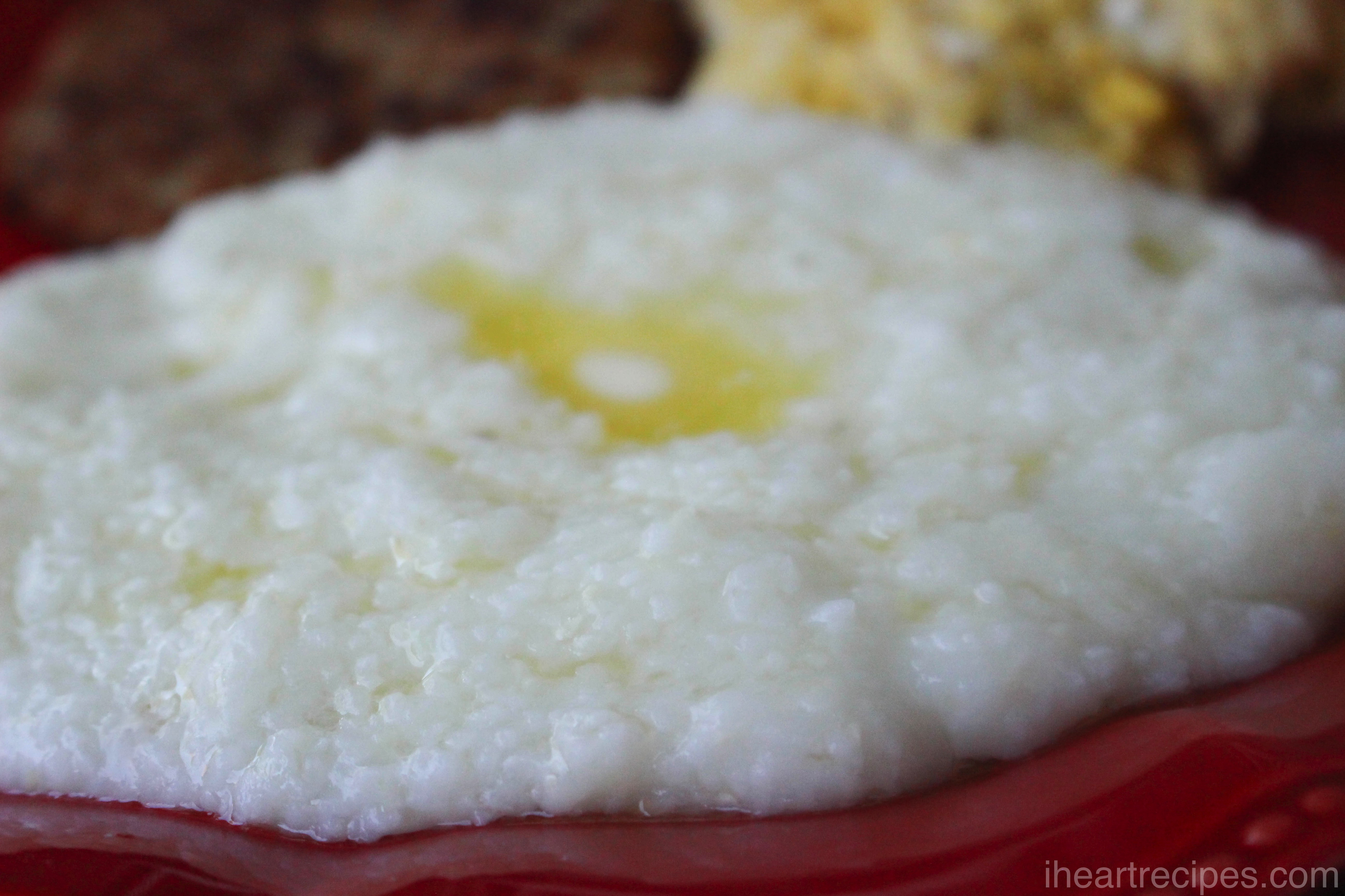 A serving of creamy grits on a red plate with a pool of melted butter in the center. 