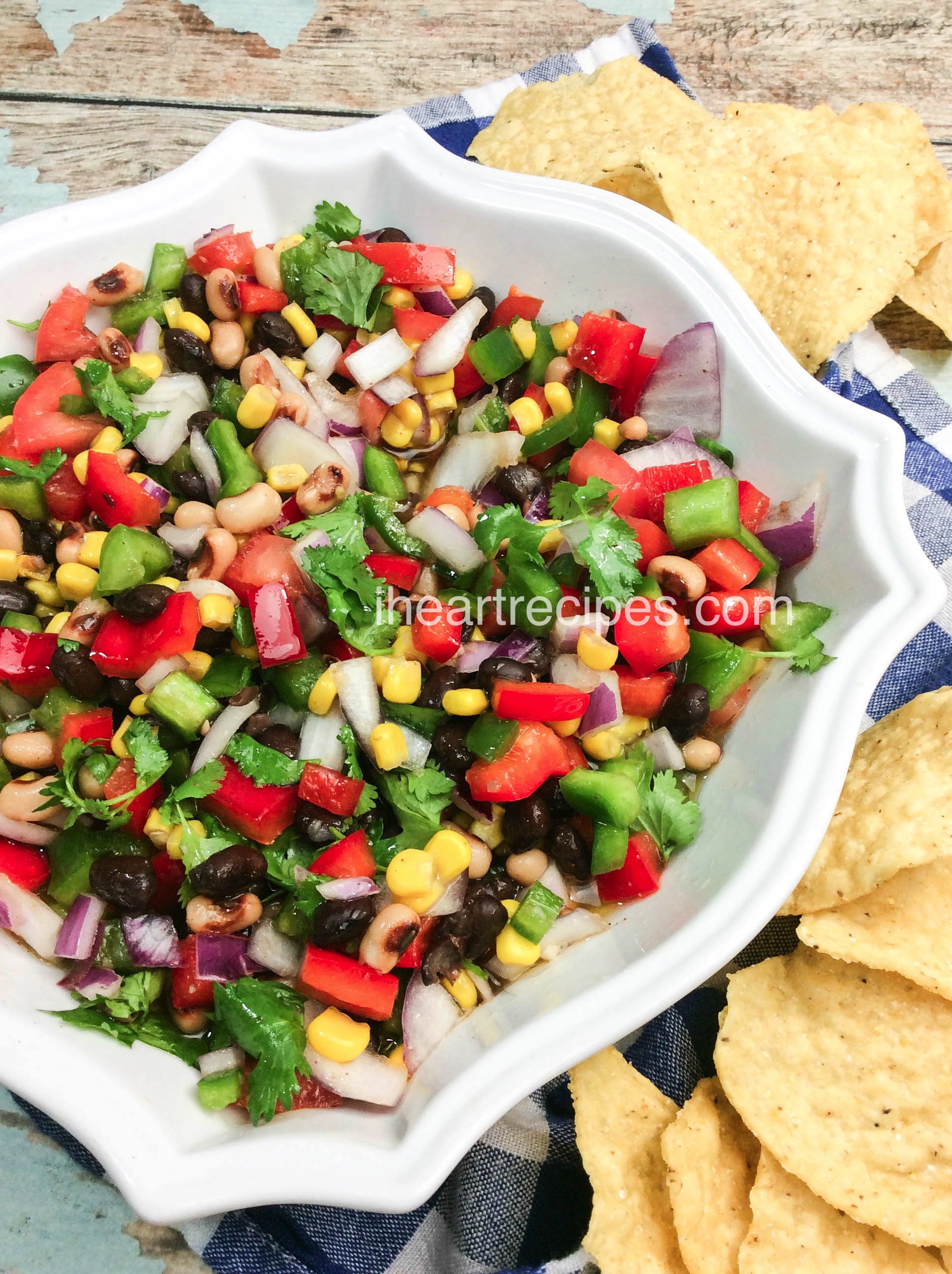 A kaleidoscope of colors and flavors fill this classic white serving bowl set atop a rustic wooden table. Serve this Texas Caviar alongside tortilla chips for a crowd-pleasing snack!