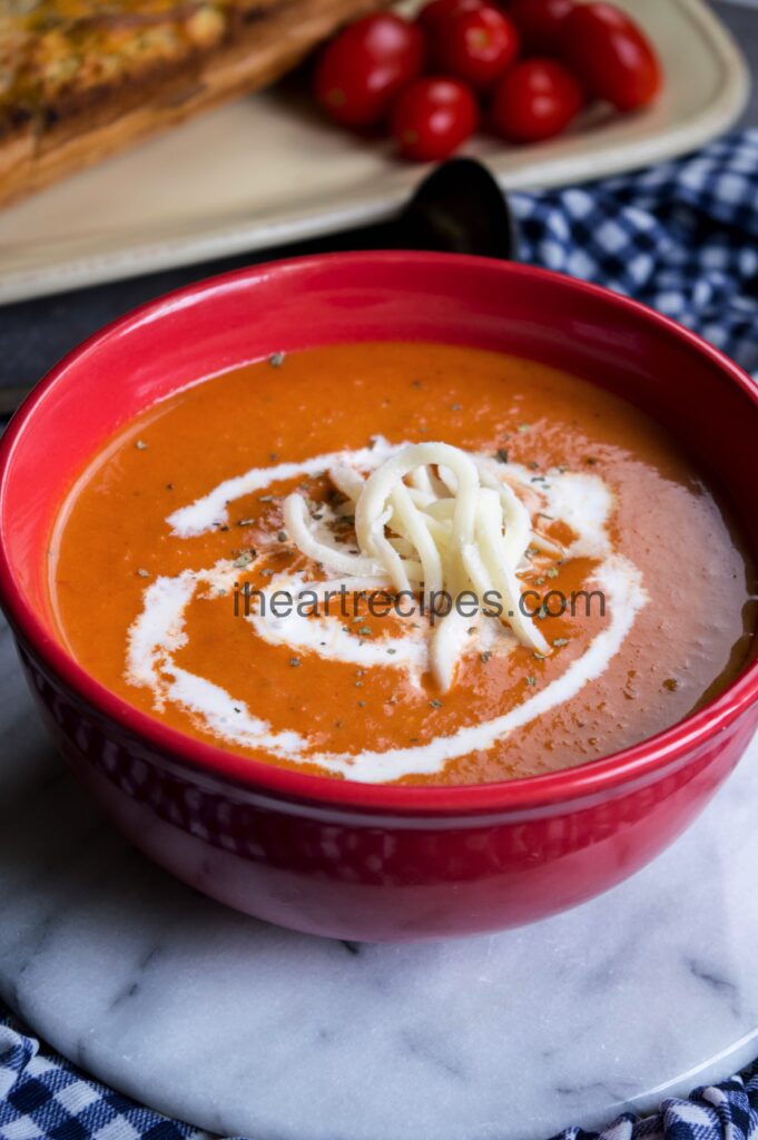 Savory tomato soup topped with sour cream, fresh cheese and seasonings served in a red bowl. 