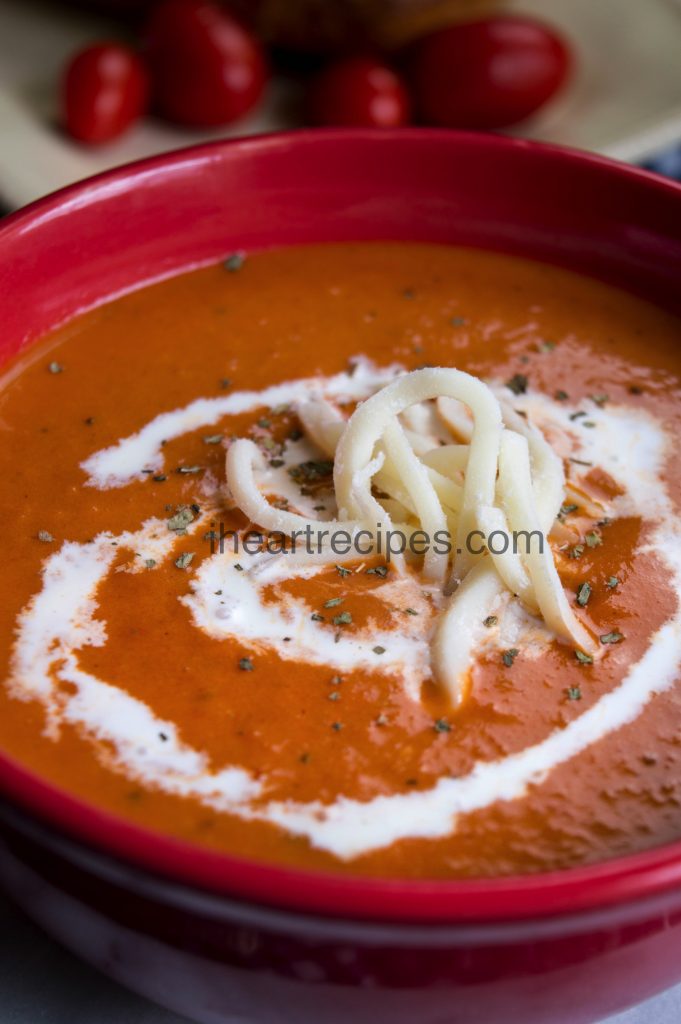 Shredded white cheese, sour cream and seasonings garnish a bowl of fresh tomato soup. 