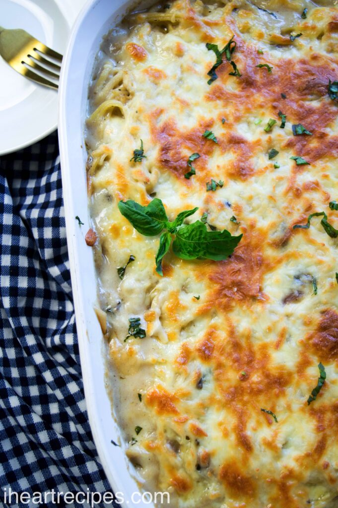 Creamy Chicken Tetrazzini topped with golden cheese and fresh basil. It's served in a white casserole dish.