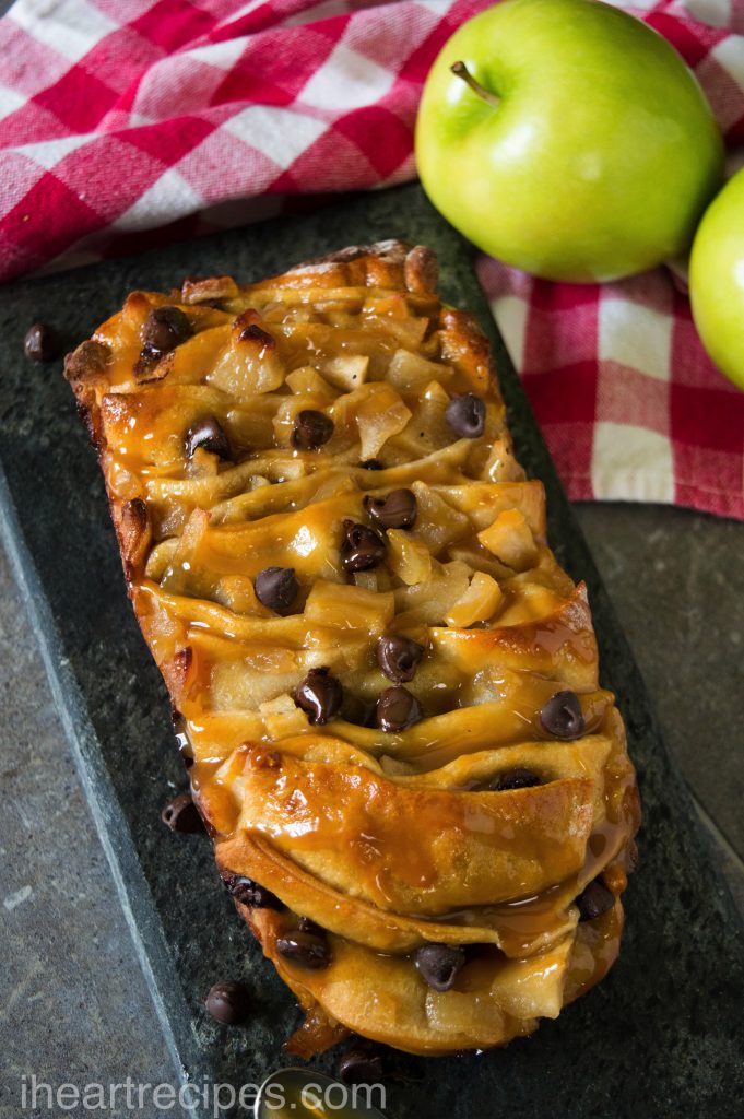Sweet and tart Caramel Apple Pull Apart Bread sprinkled with chocolate chips and served on a stone platter. Two green apples on a red and white gingham towel are nearby. 