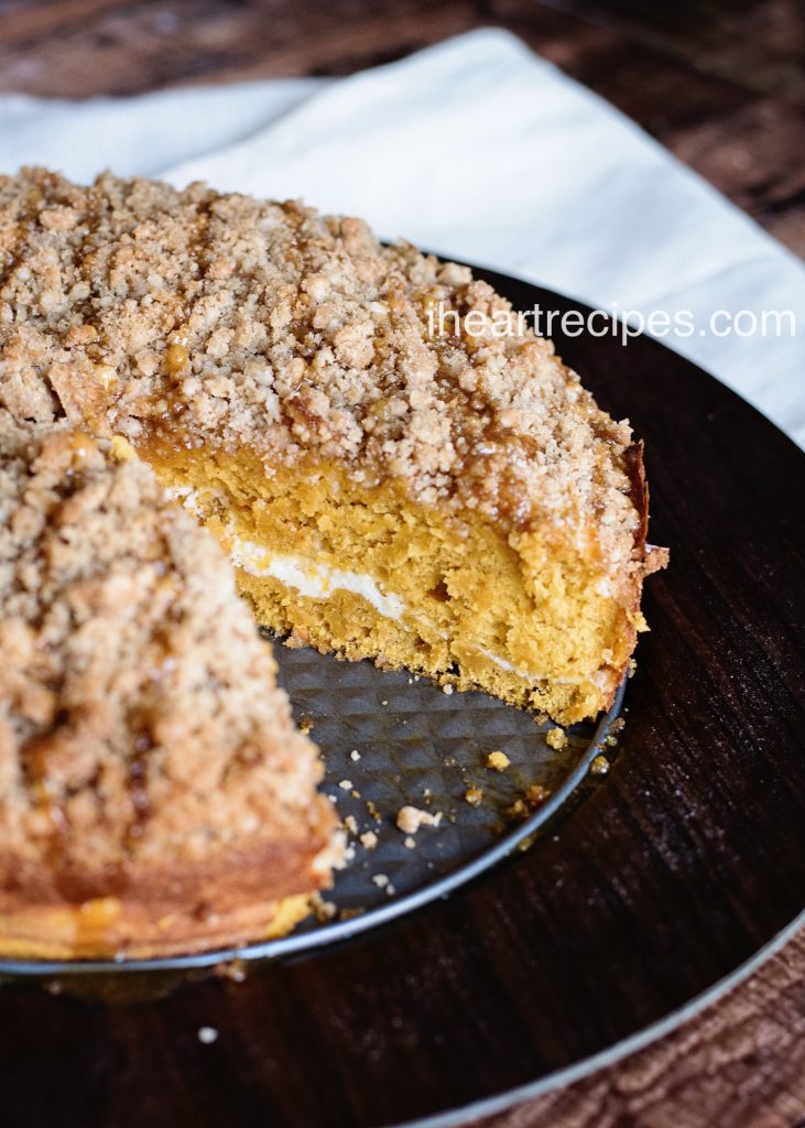 A slice of caramel pumpkin coffee cake is removed from the pan showing layers of moist cake, cream cheese filling and sweet crumble topping.