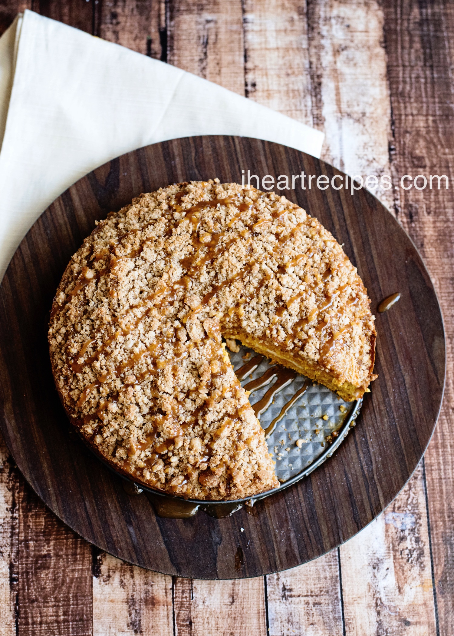 A delicious caramel pumpkin caramel cake drizzled with sweet caramel topping sits on a rustic wood serving platter. Enjoy a slice of this delicious fall dessert.