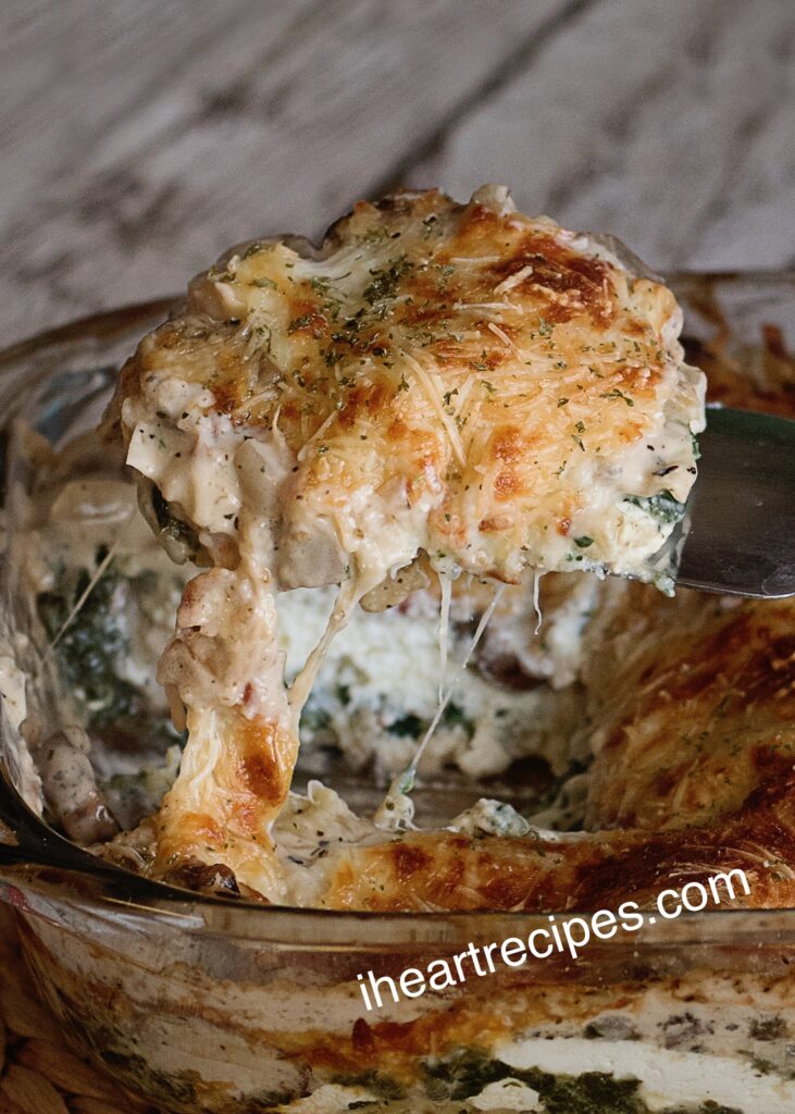 A slice of vegetable lasagna topped with creamy cheese is pulled from a casserole dish with a spatula. 