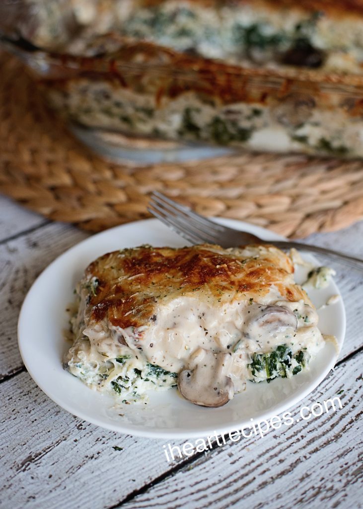 A single slice of homemade vegetarian lasagna sits on a white plate. The white sauce lasagna is made with a creamy alfredo sauce and packed with layers of spinach, mushrooms, and lasagna noodles.