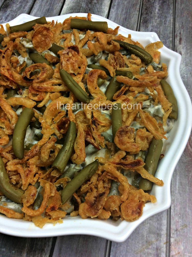 A semi-homemade green bean casserole in a white ceramic dish. The creamy green bean casserole is topped with crispy fried onions.