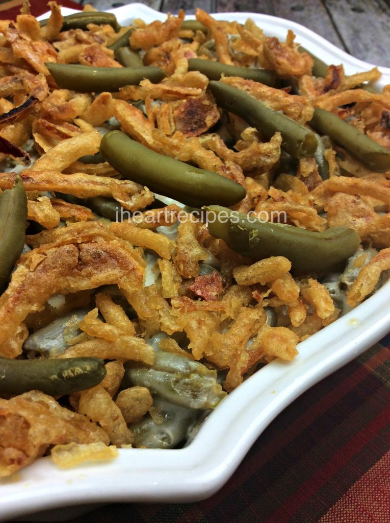 A close-up look at a casserole dish filled with green bean casserole. The French-cut green beans are baked in a cream of chicken cream sauce and topped with crispy golden-brown fried onions.