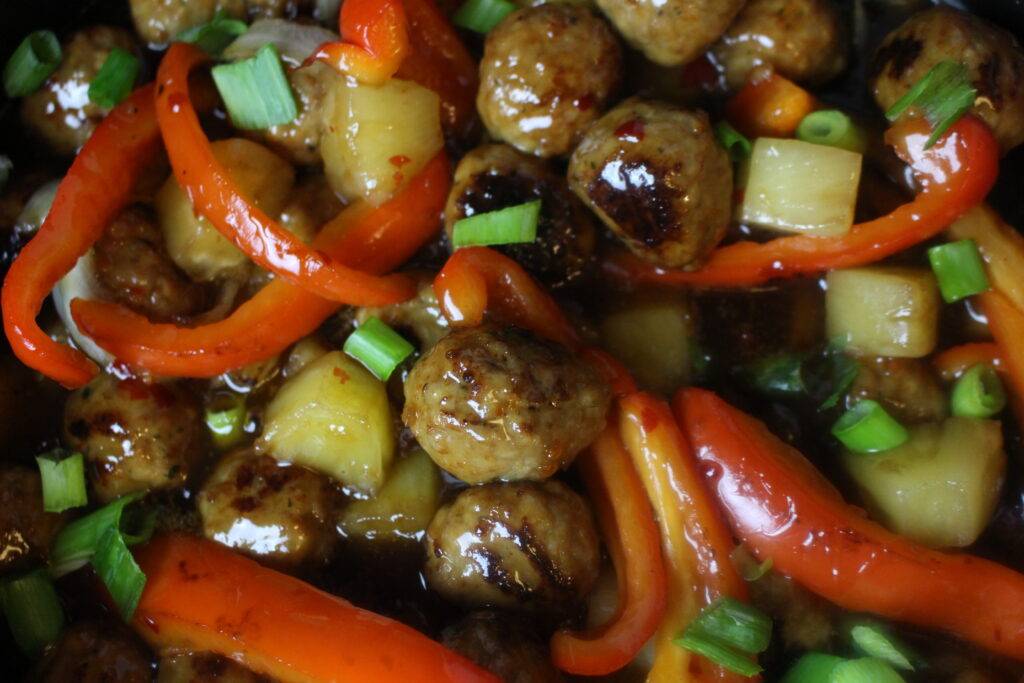 A close up of savory Sweet & Sour Meatballs mixed with delicious sweet peppers and tender pineapple chunks in a tangy glaze!