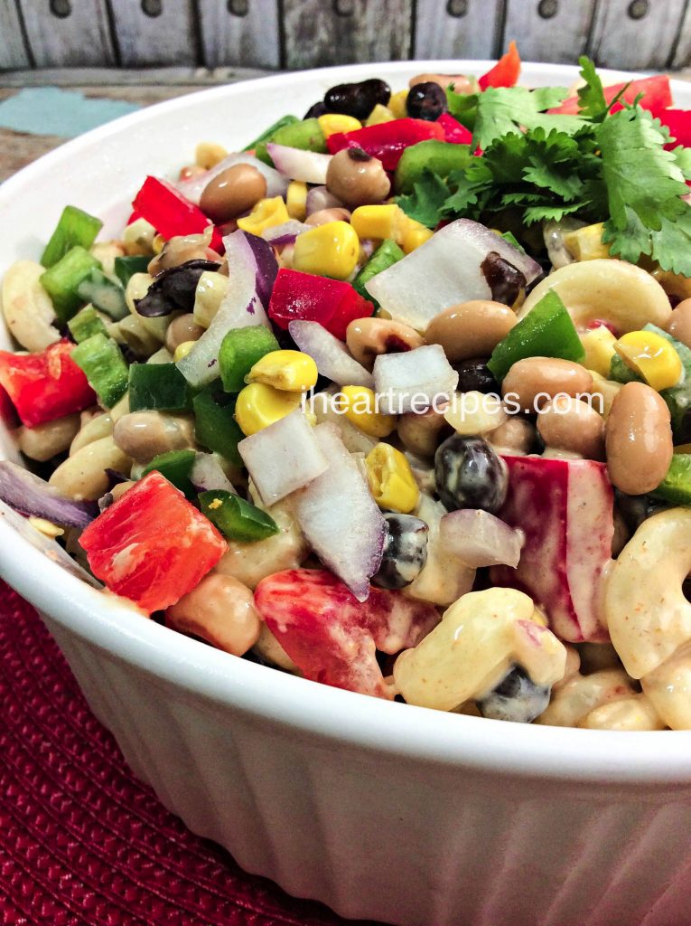 A classic white bowl filled with savory Texas Caviar Macaroni Salad and garnished with fresh cilantro. It is a perfect crowd-pleasing summer pasta salad.